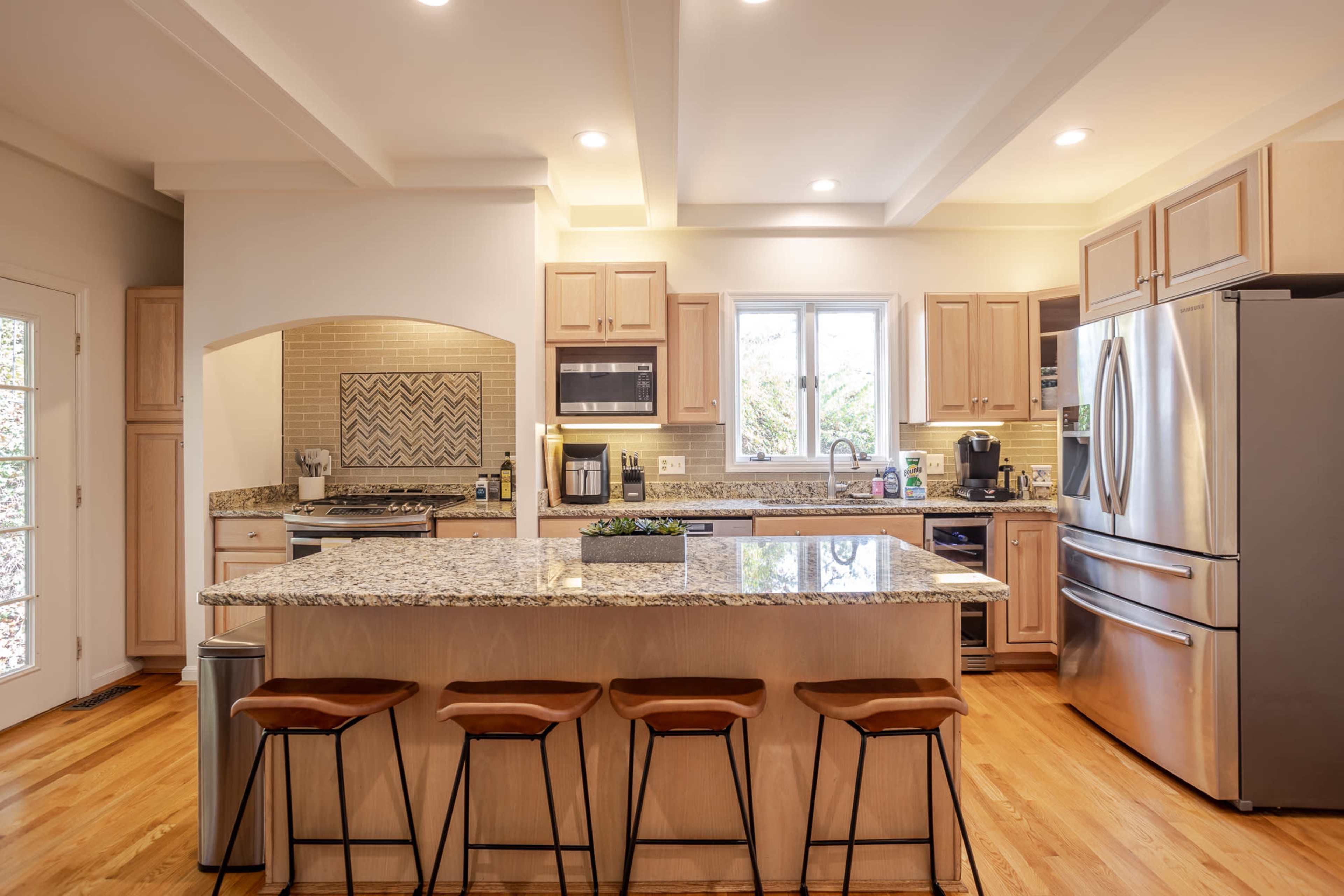 A modern kitchen features wood cabinetry, stainless steel appliances, and a central island with seating.