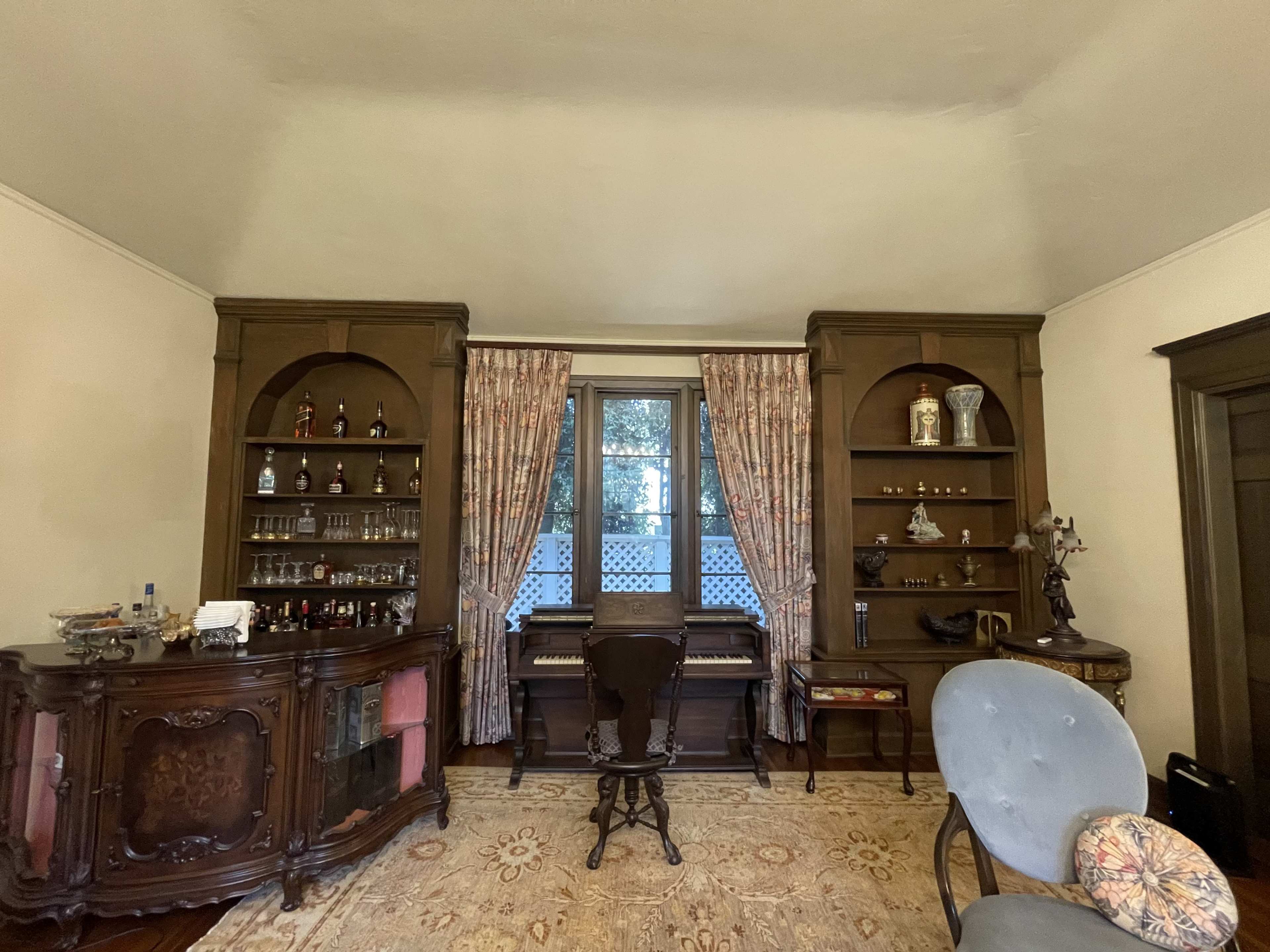 A vintage room featuring a grand piano flanked by wooden shelves with decorative items and a small bar area.