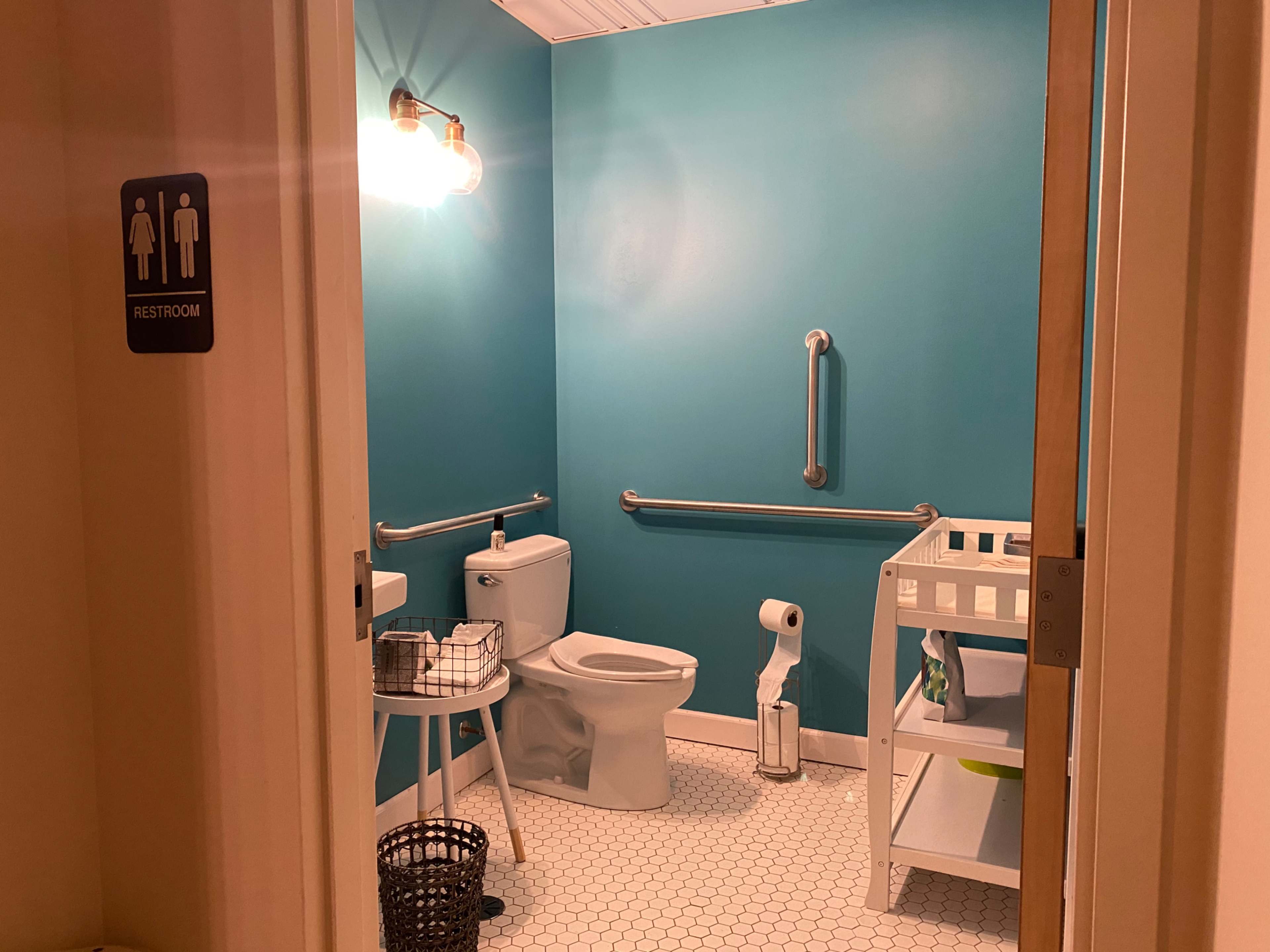 A small restroom with a bright blue wall, featuring a toilet, a changing table, and a basket on a nearby table.