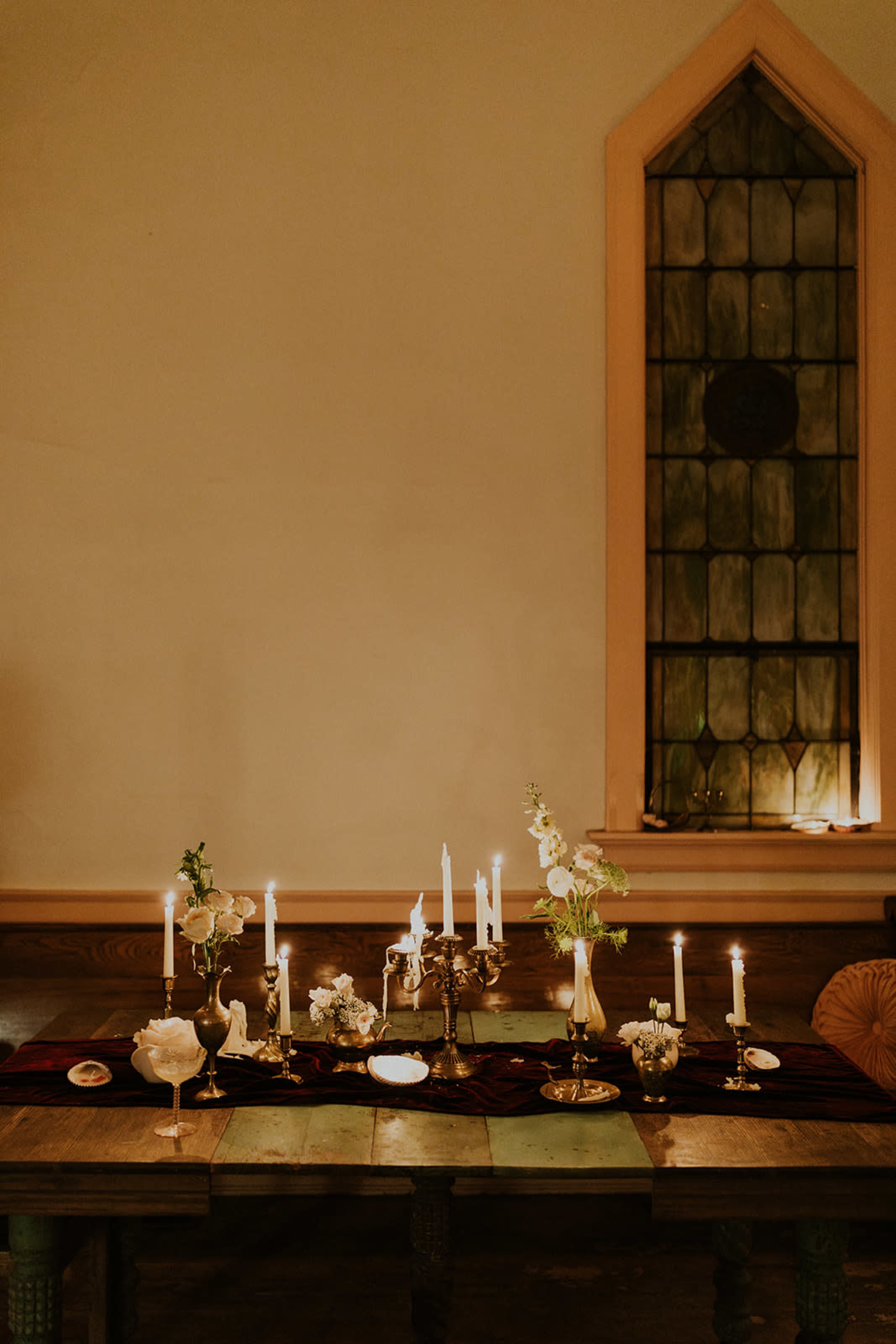 The scene features a dimly lit table set with candles, floral arrangements, and decorative dishes, positioned next to a stained glass window.