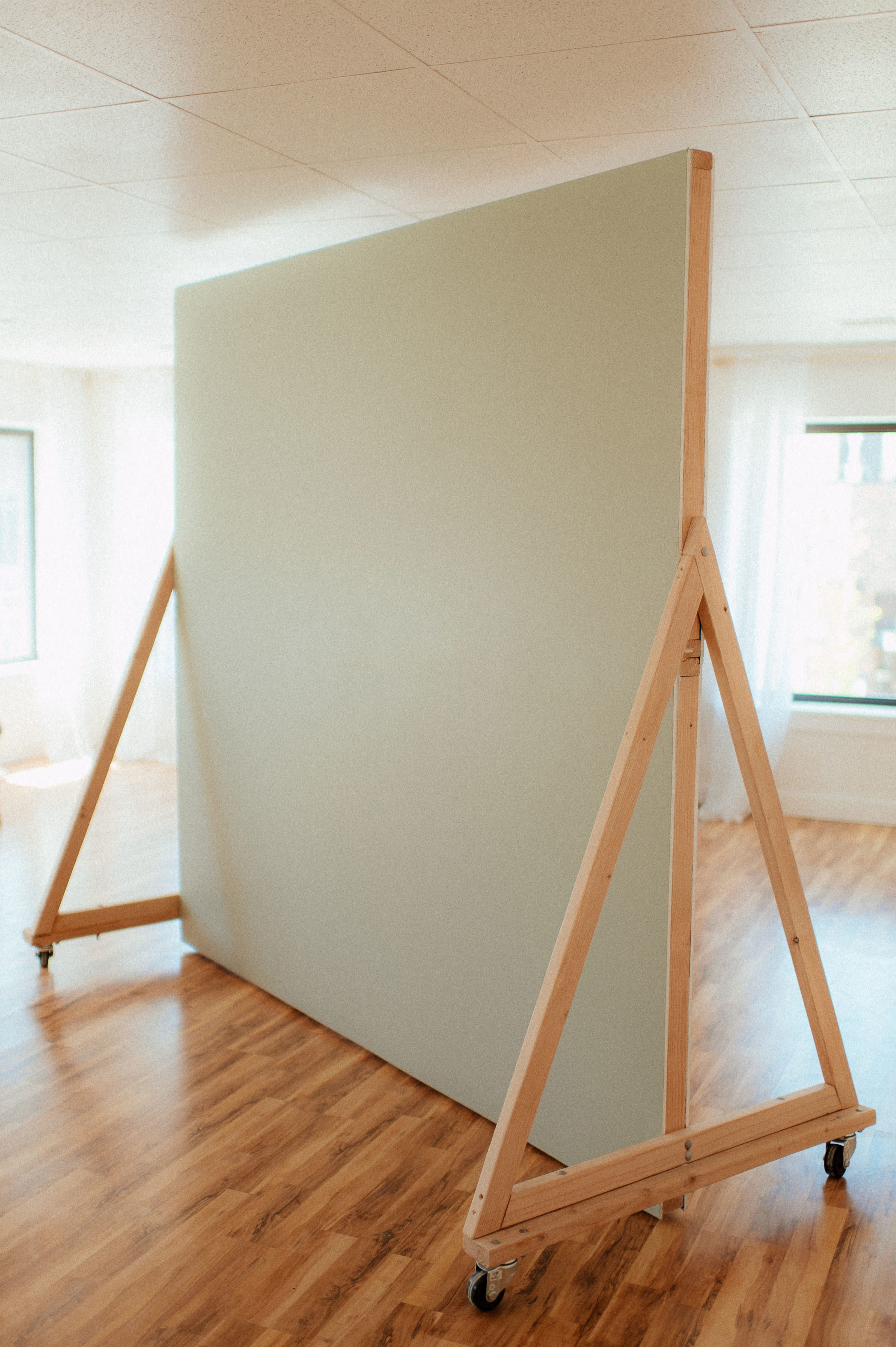 A large, portable, green partition stands on wooden supports with wheels in a well-lit room.