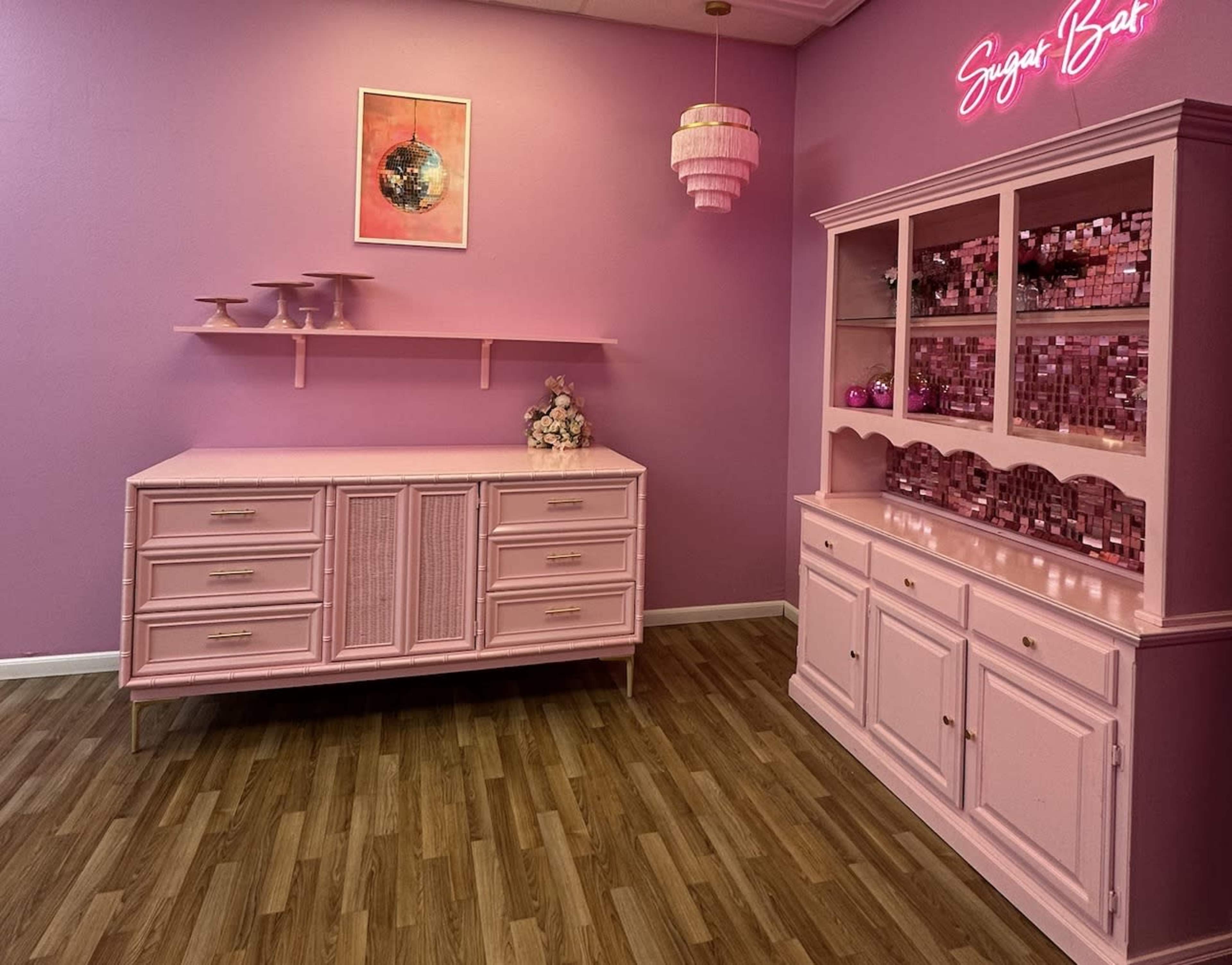 The room features a pink theme with a dresser and a display cabinet, both adorned with decorative items and wall art.
