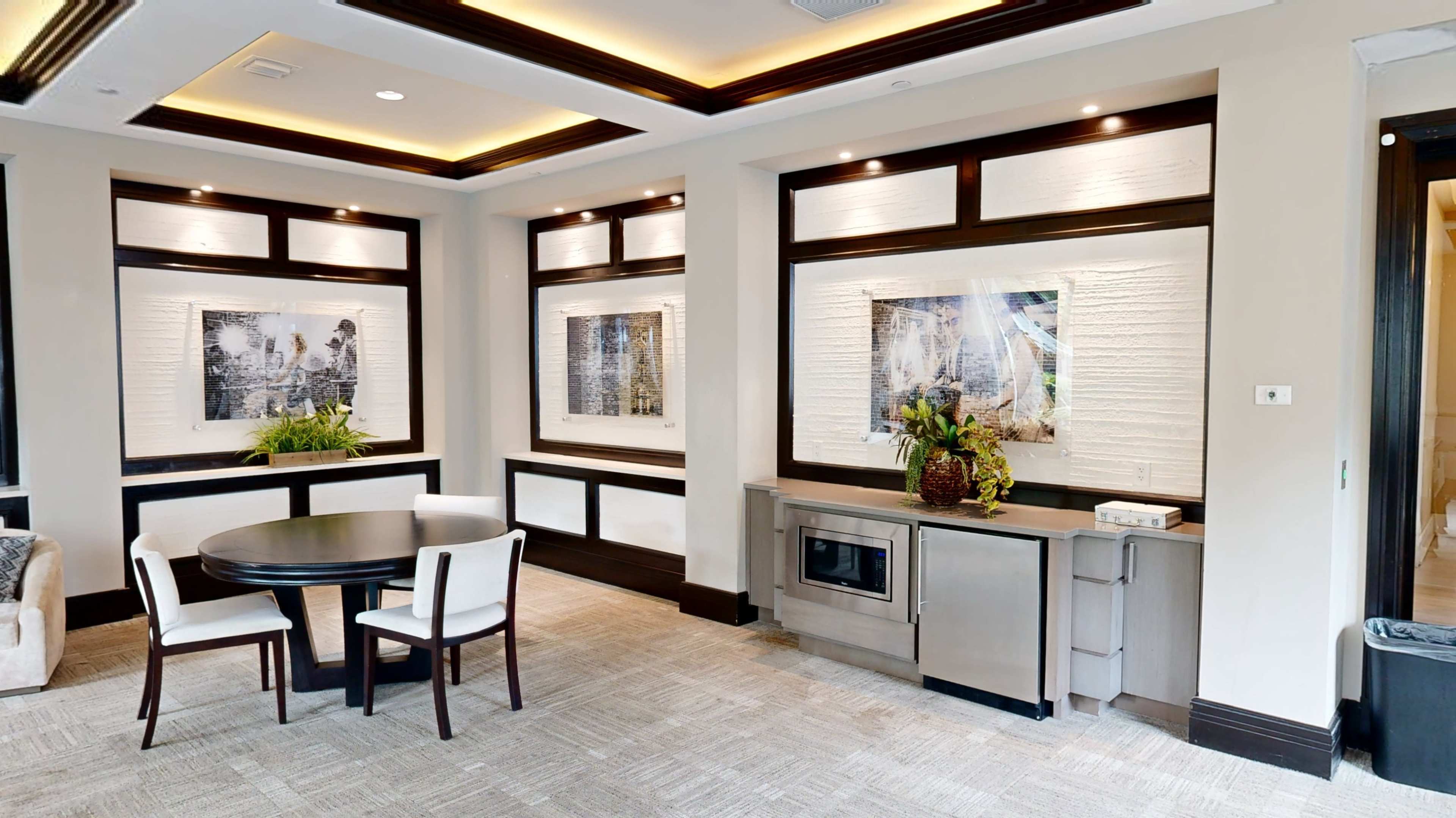 A modern interior space with a round table and chairs, framed artwork on the walls, and a built-in microwave unit.