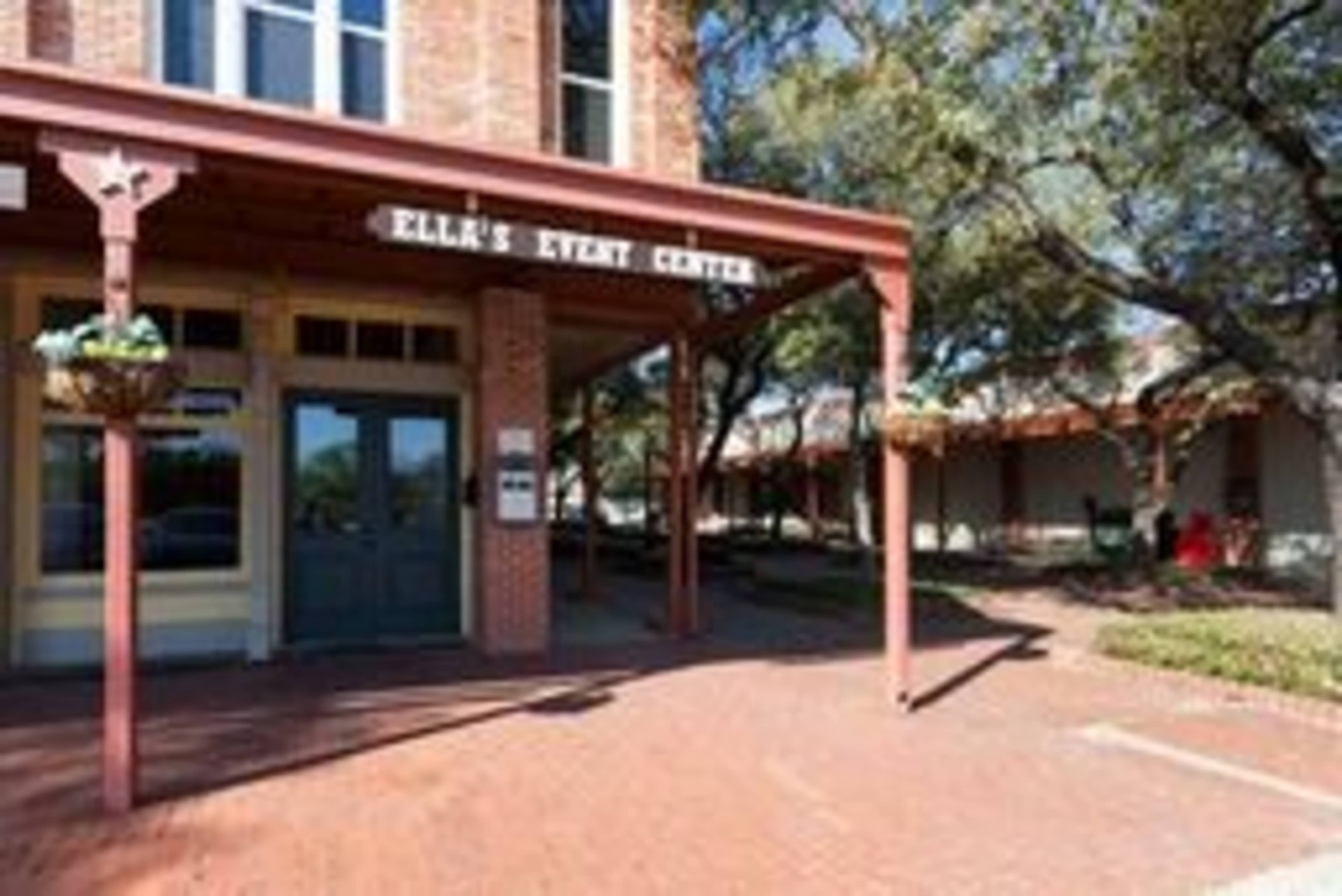 The entrance of Ella's Event Center features a wooden overhang and brick walkway, surrounded by trees and landscaping.