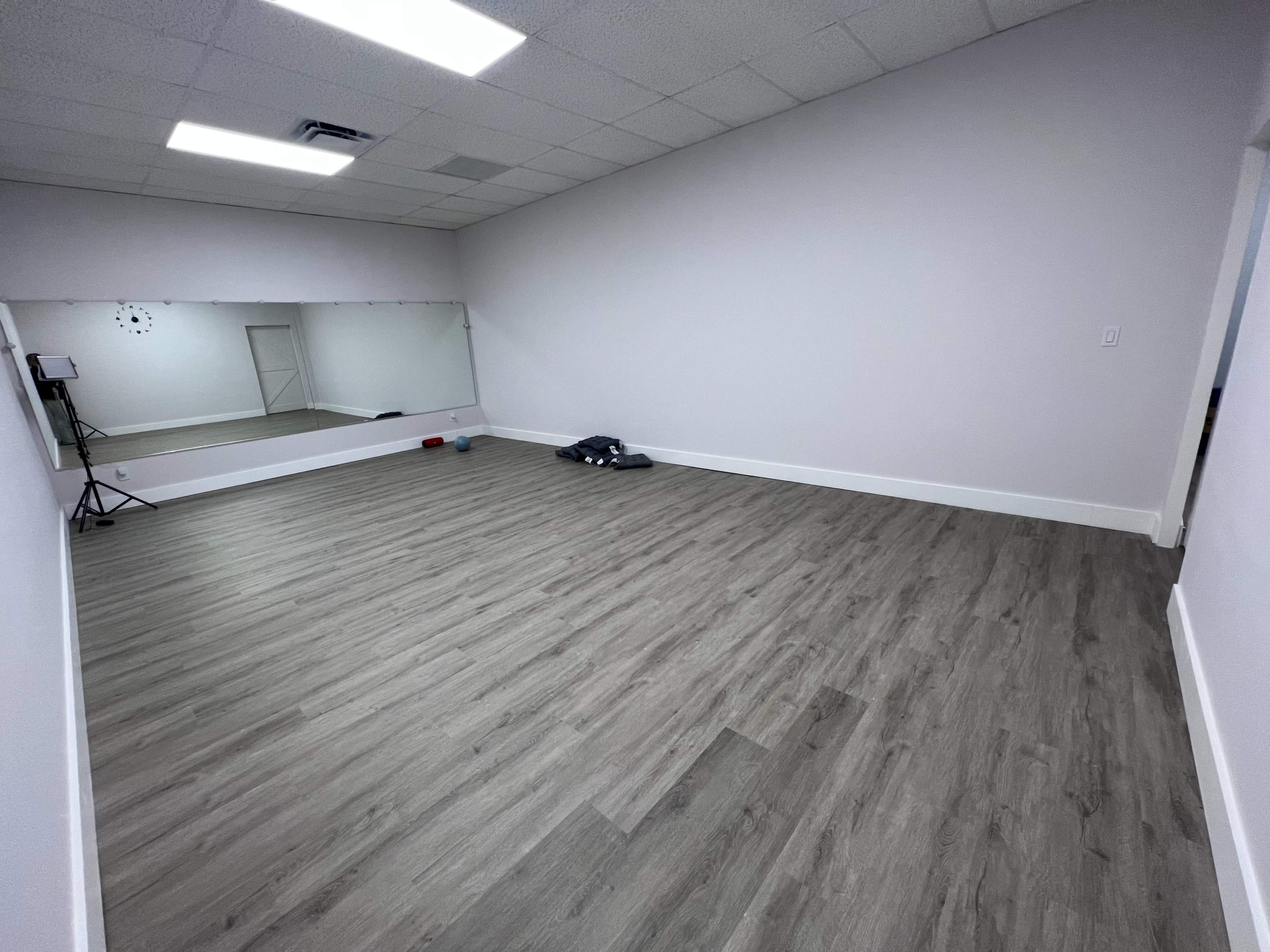 A spacious, empty room with wooden flooring and a large mirror on one wall.