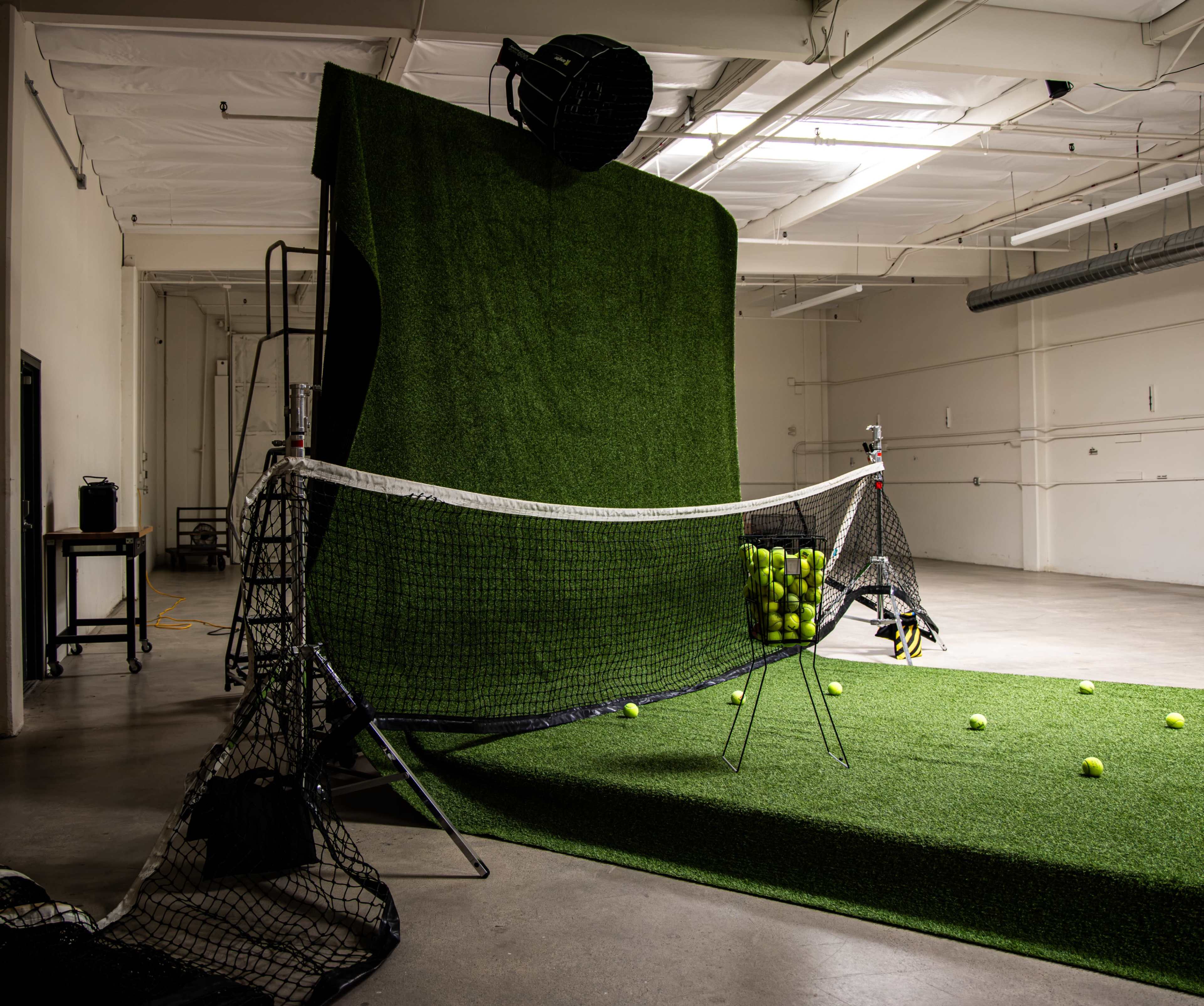 The image shows a driving range setup with a large artificial turf hitting area, a netted enclosure, and several golf balls scattered on the ground.