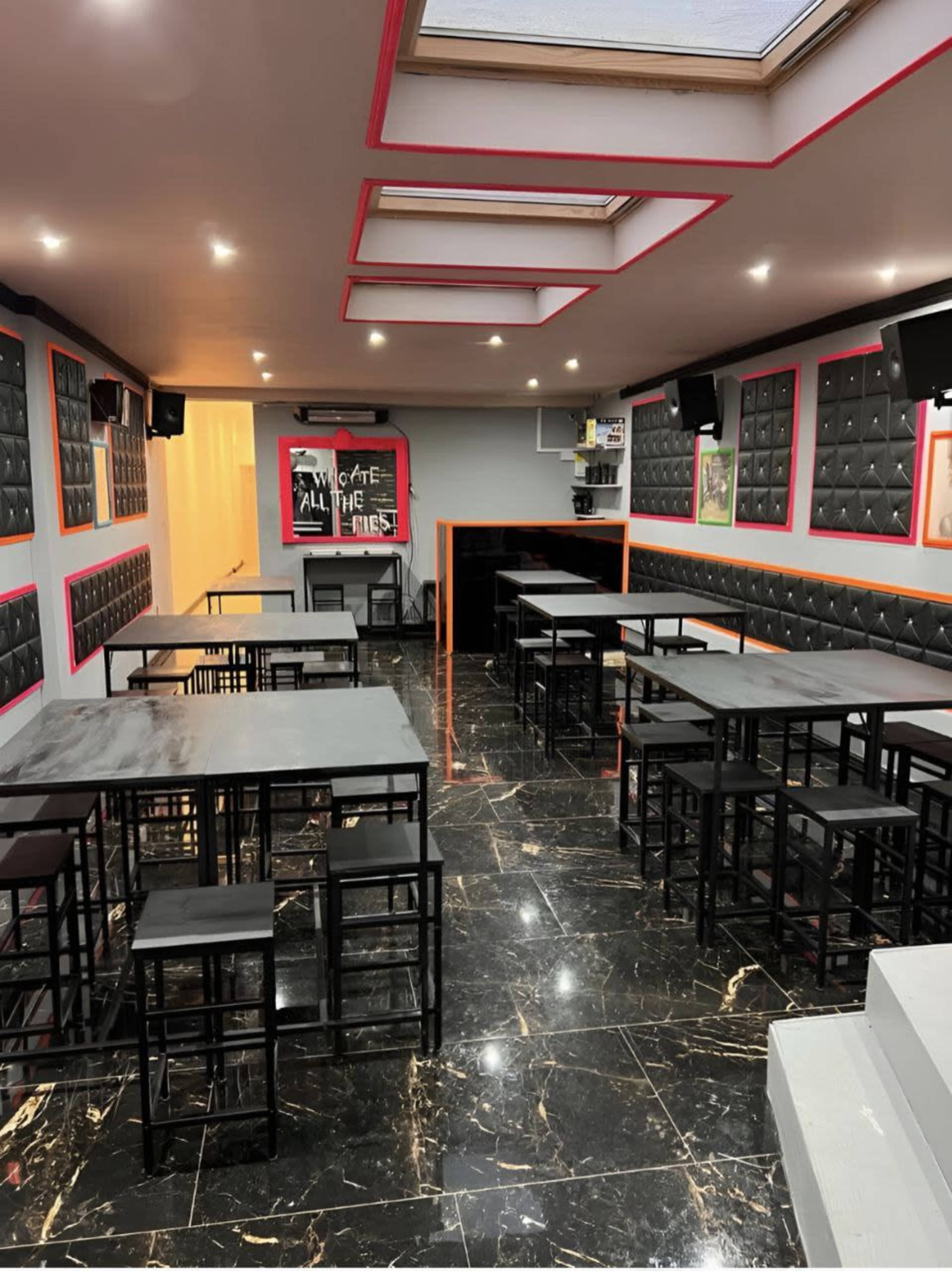 A modern interior of a restaurant or café with black marble flooring, several tables and chairs, and skylights in the ceiling.