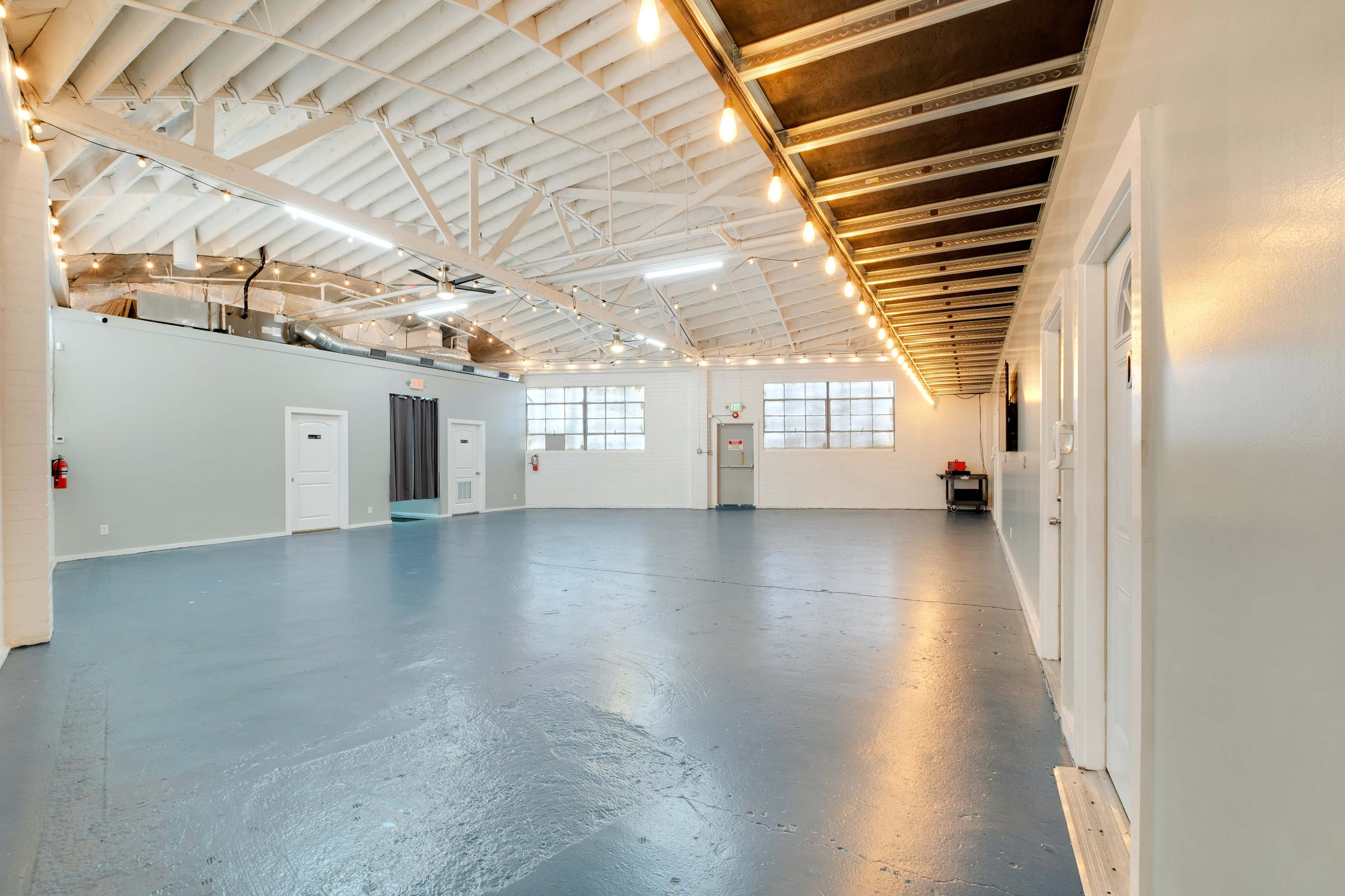 A spacious, well-lit industrial interior with high ceilings, a polished floor, and several doors along the walls.