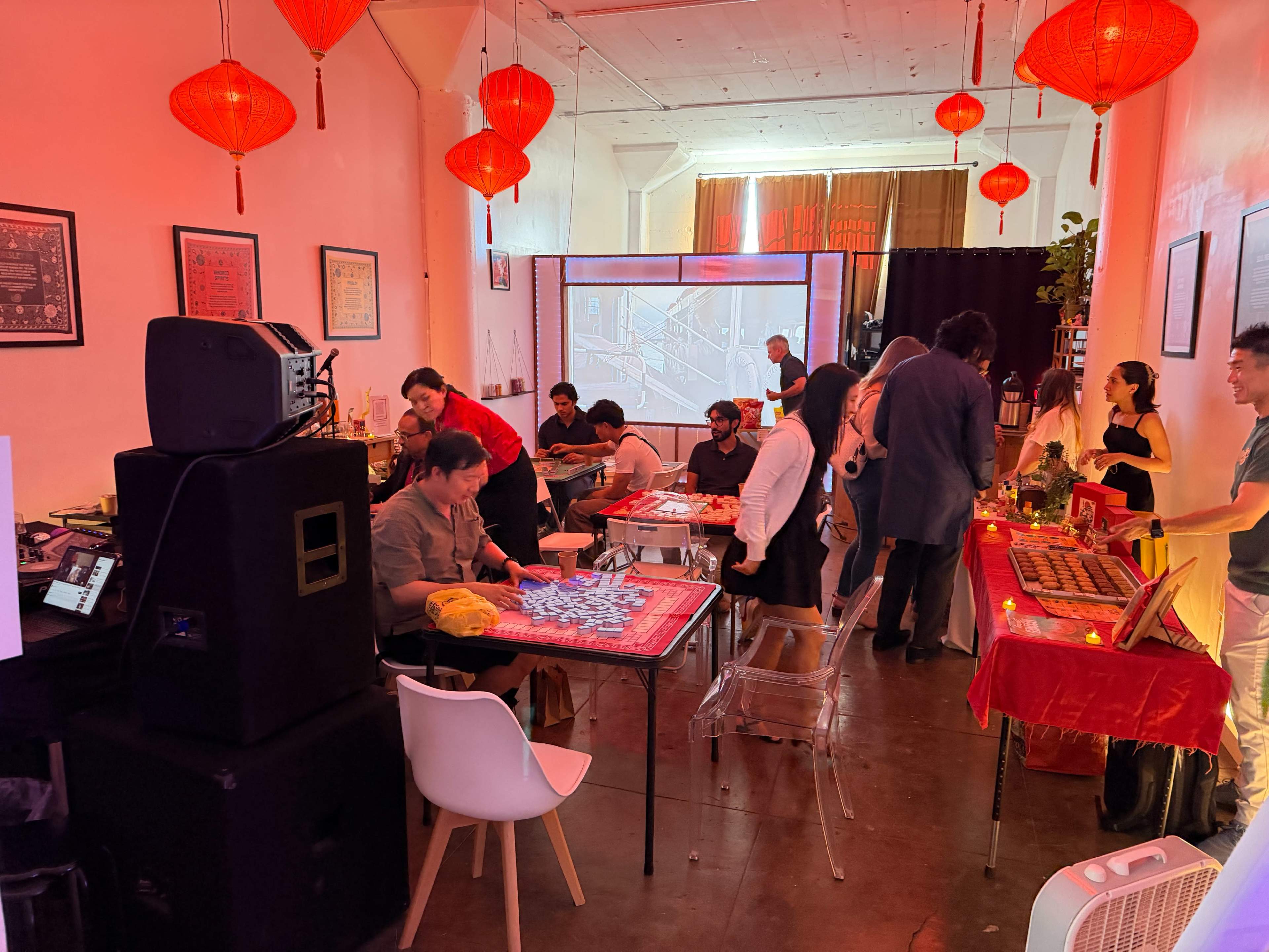 The scene depicts a festive indoor gathering with people engaged in various activities, surrounded by red lanterns and decorated tables.
