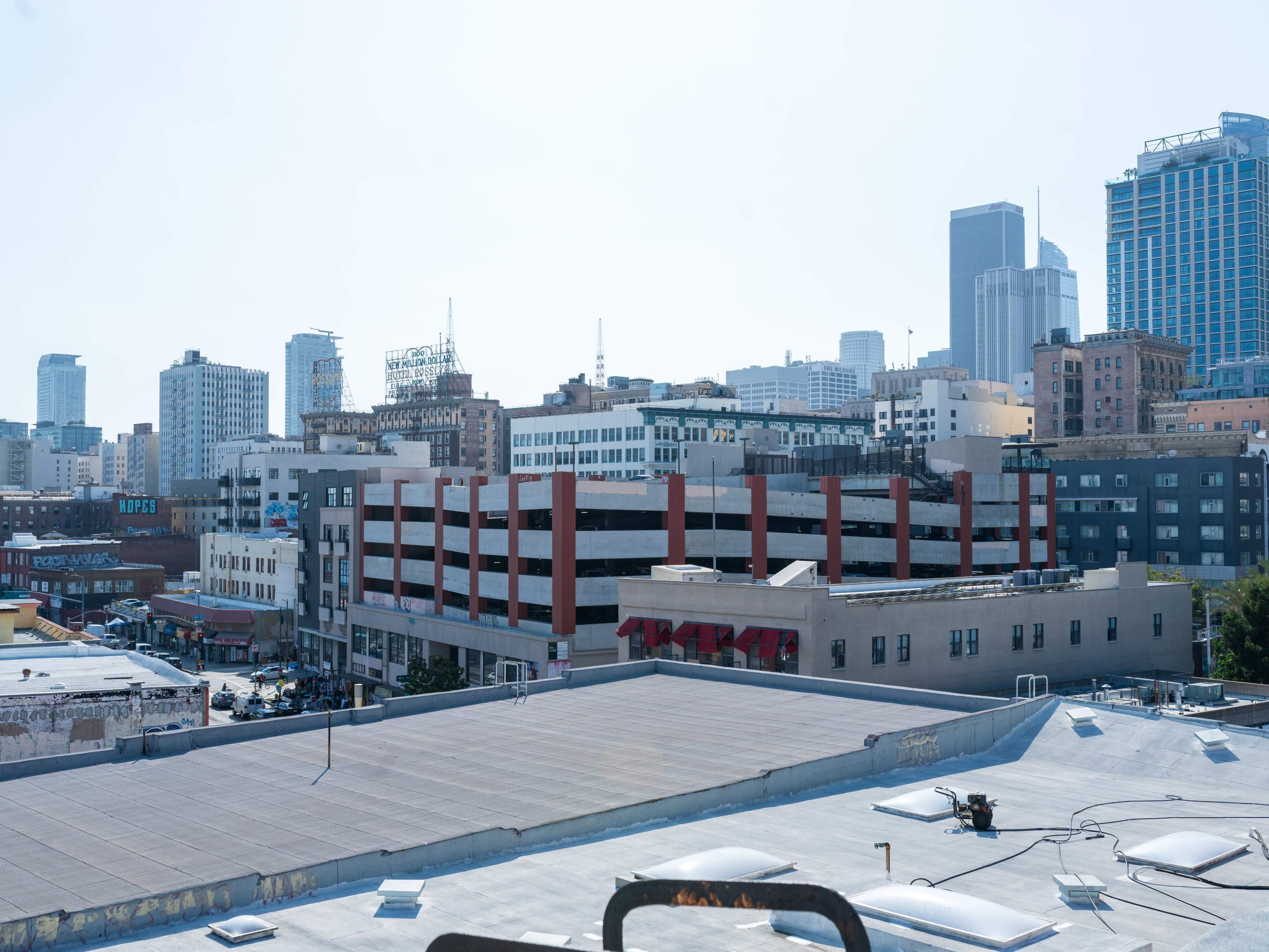 The image shows a city skyline with a mix of modern and older buildings, including a parking structure in the foreground.
