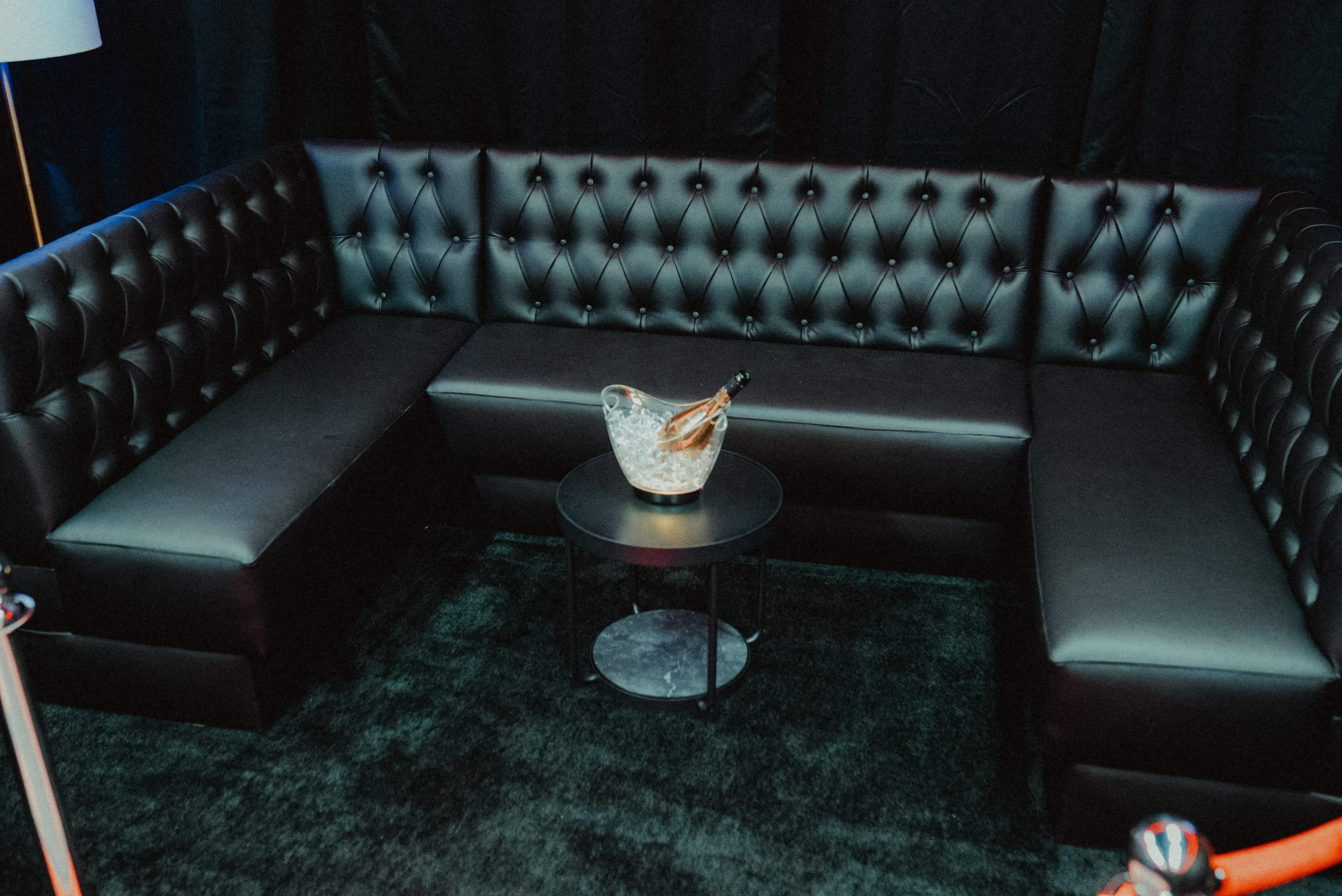 A black leather sectional sofa arranged in a corner, accompanied by a small round table holding a bucket of ice with a bottle.