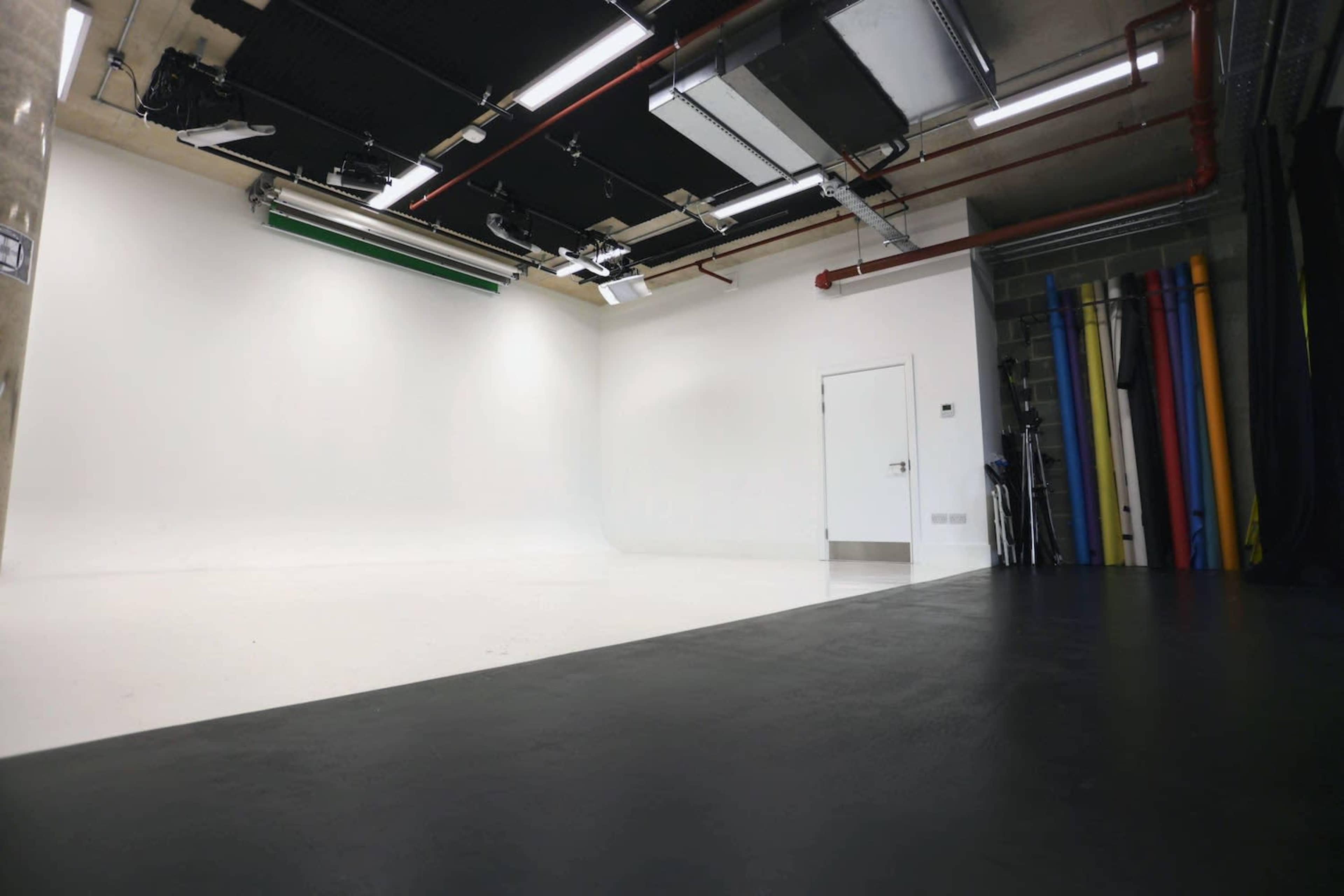 A minimalistic studio space with a white backdrop, a door, and colorful backdrop rolls arranged against a wall.