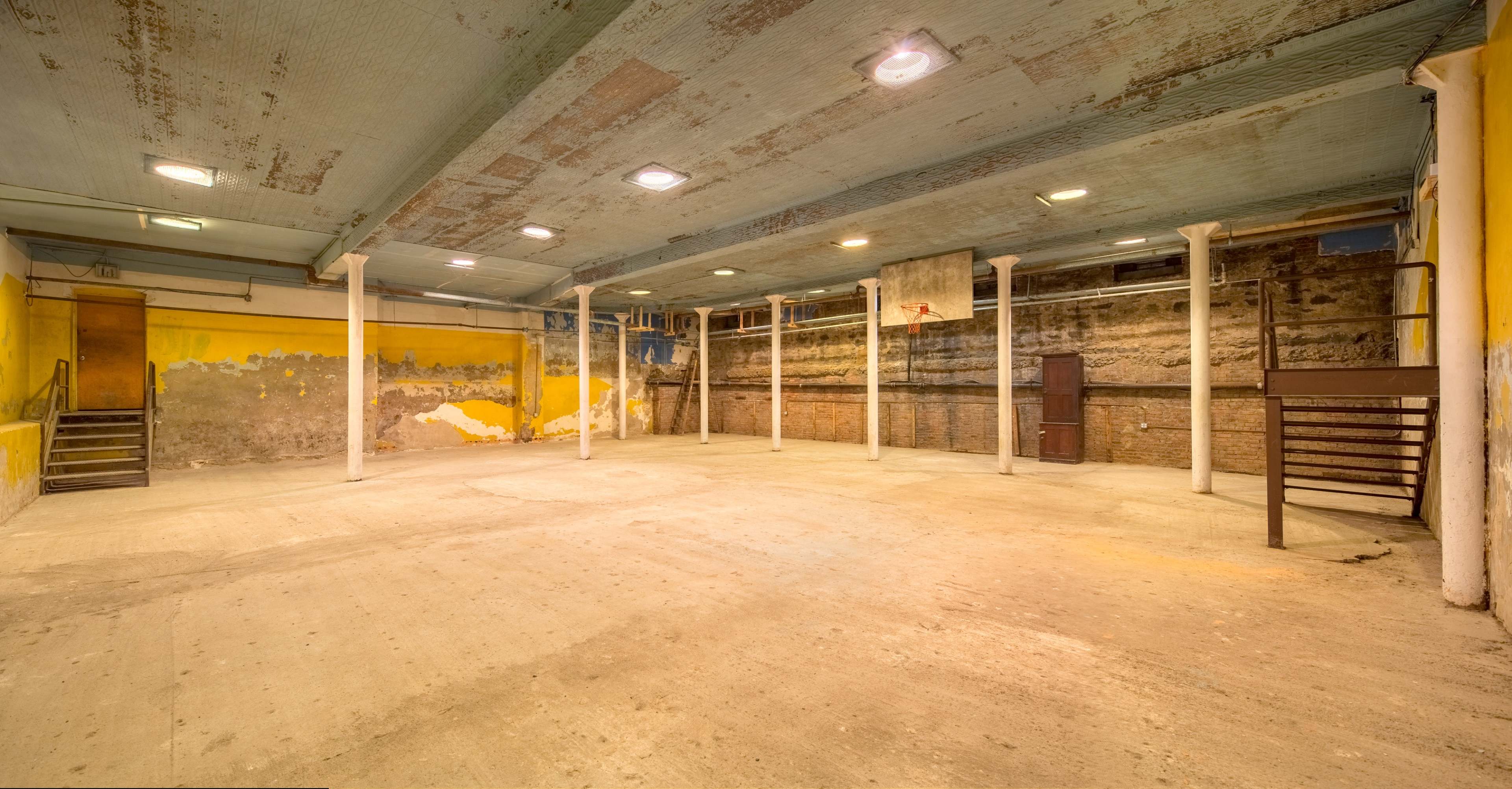 An empty indoor basketball court with bare walls, concrete flooring, and several tall columns supporting the ceiling.