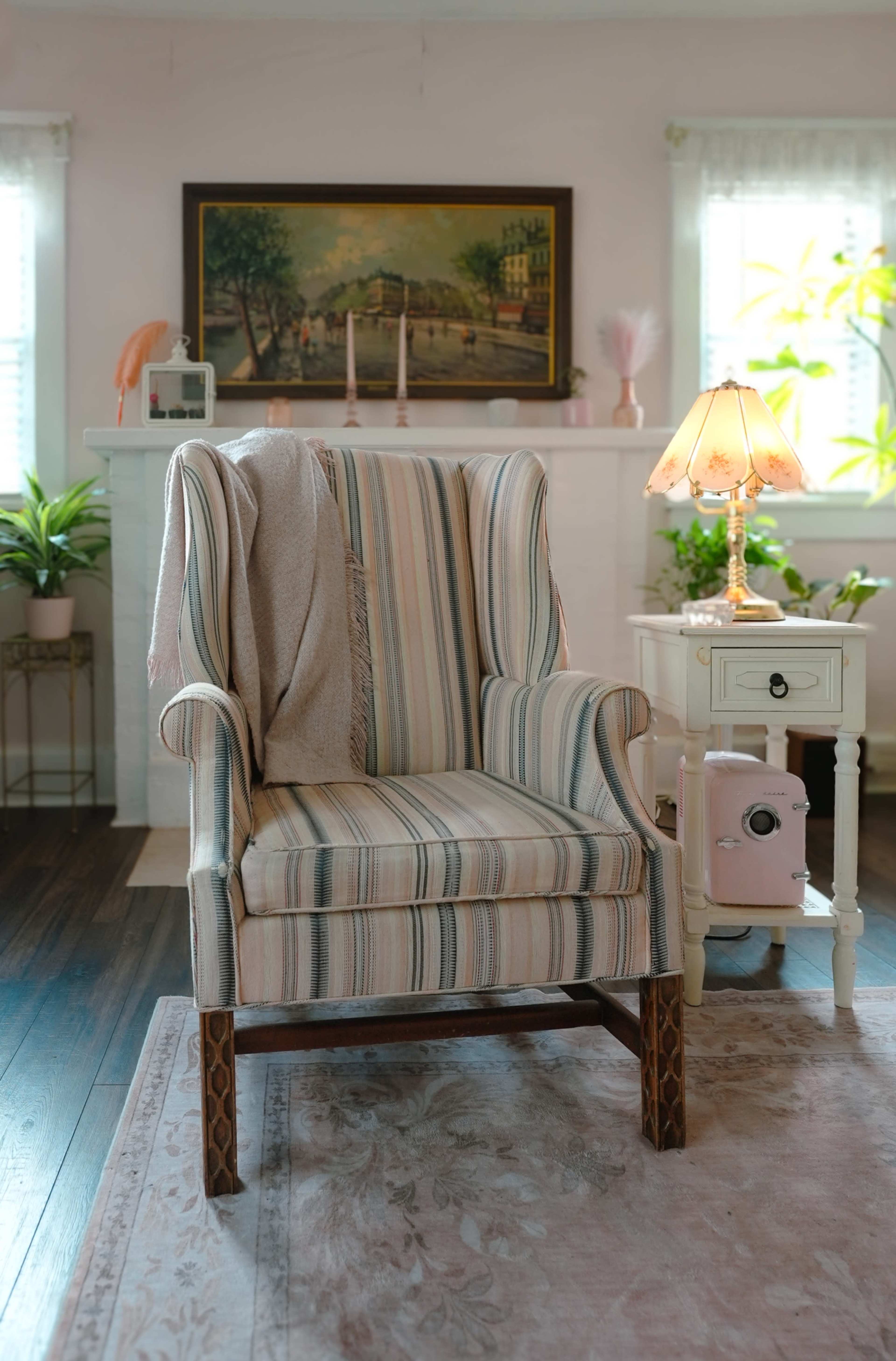 The image shows a striped armchair with a blanket draped over it, positioned next to a small table and a lamp in a well-lit living room.