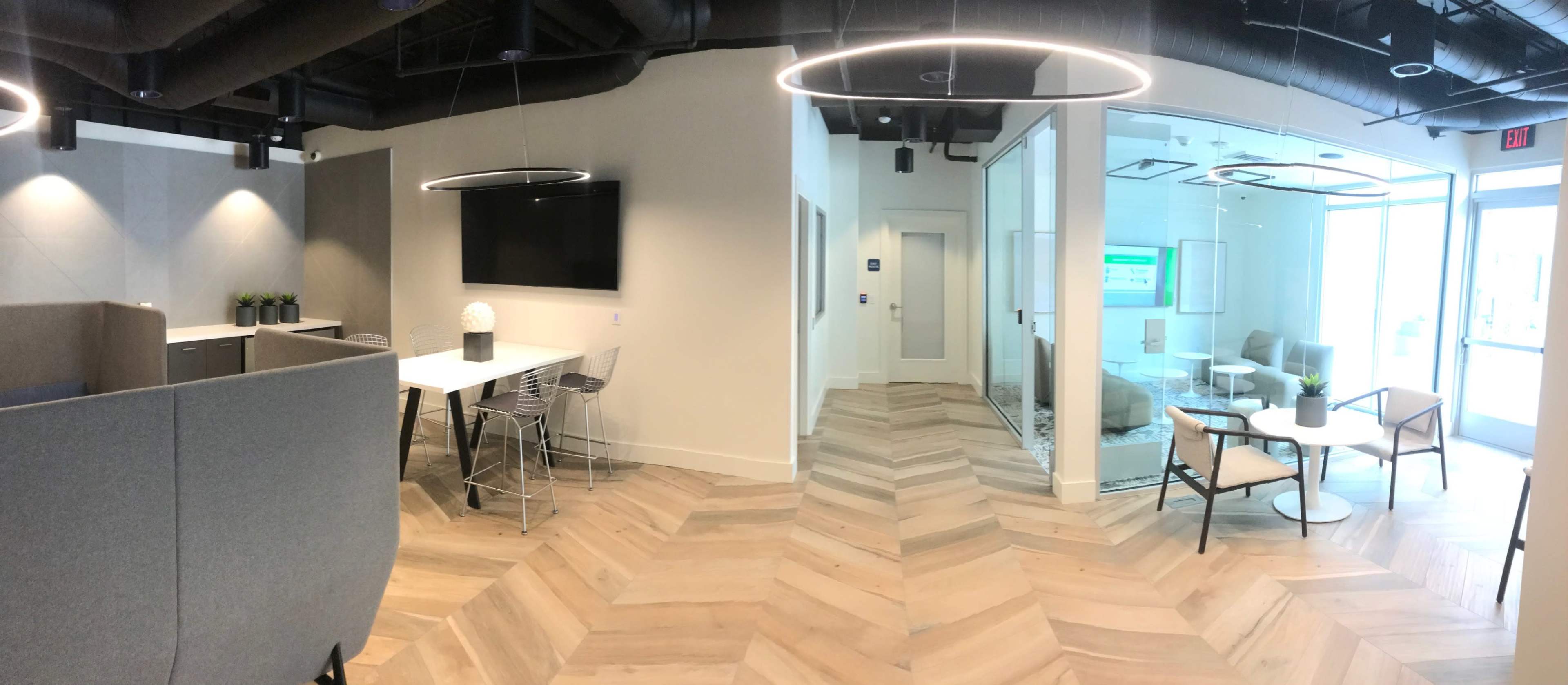 A modern office space featuring a mix of workstations, a meeting area, and lounge seating with a herringbone-patterned floor.