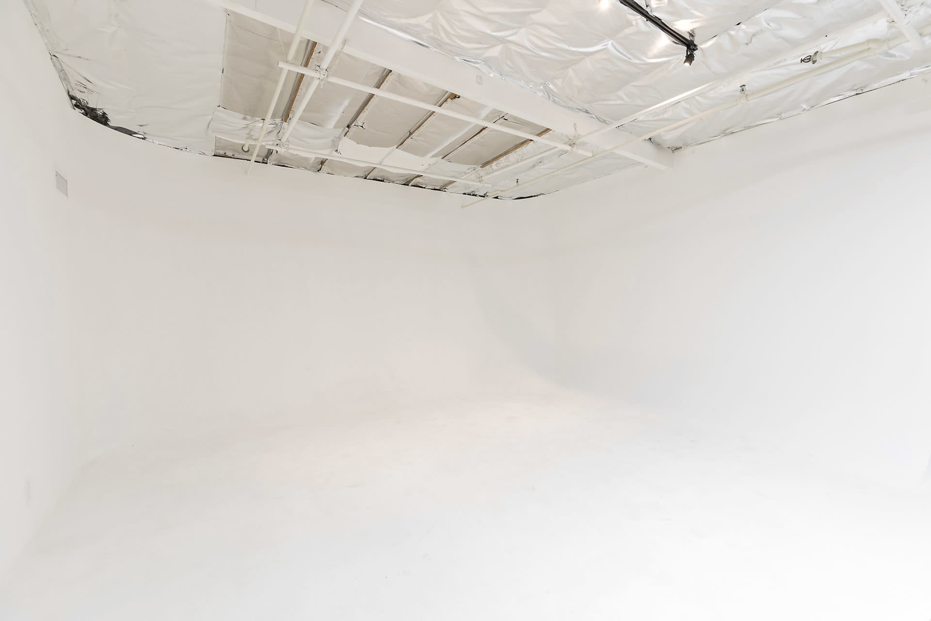 The image shows an empty white room with a smooth floor and a ceiling partially covered in metallic material.