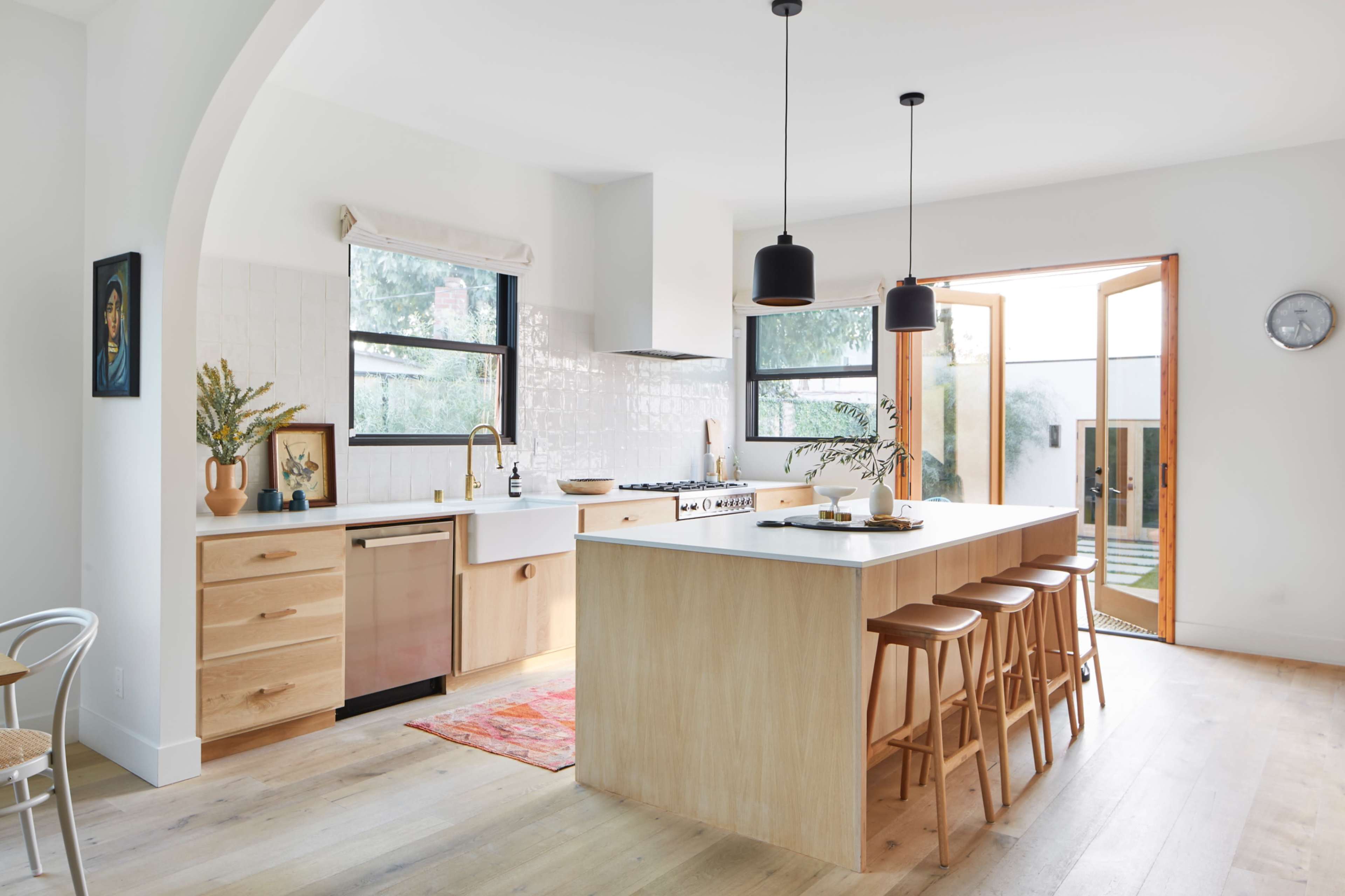 A modern kitchen features a large island with bar stools, wooden cabinetry, and an open doorway leading to an outdoor area.