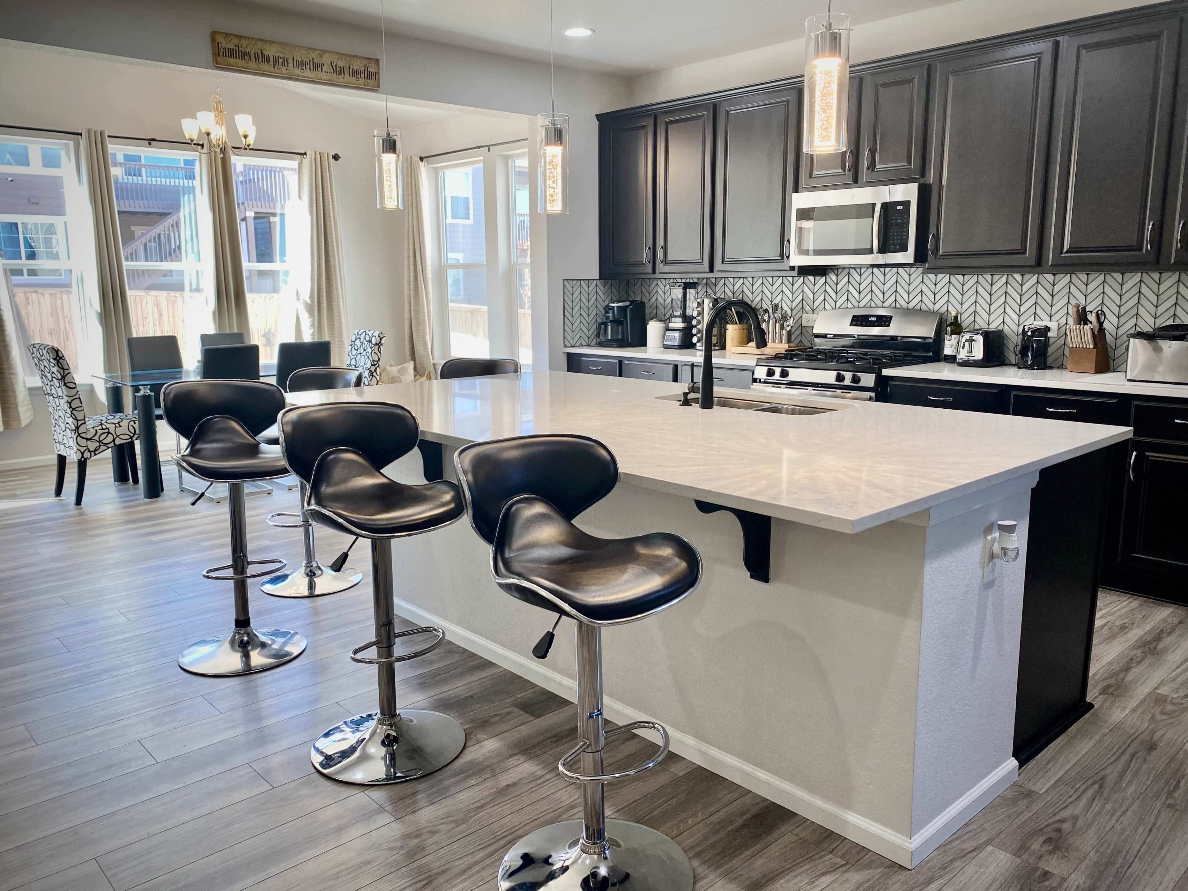 A modern kitchen features dark cabinetry, a large island with bar stools, and stainless steel appliances.