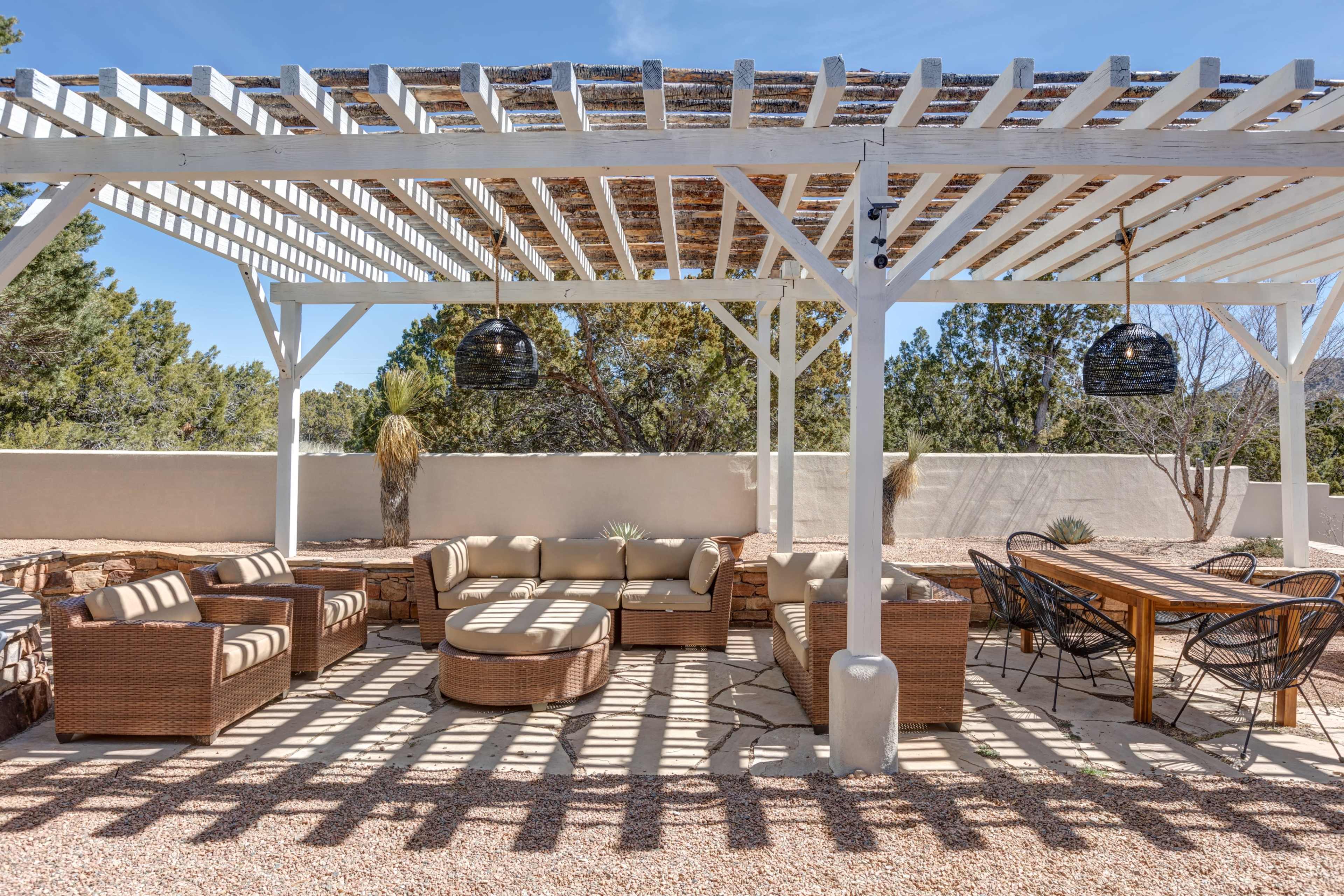 A spacious outdoor patio features a pergola with overhead lattice, surrounded by wicker seating and a long dining table.