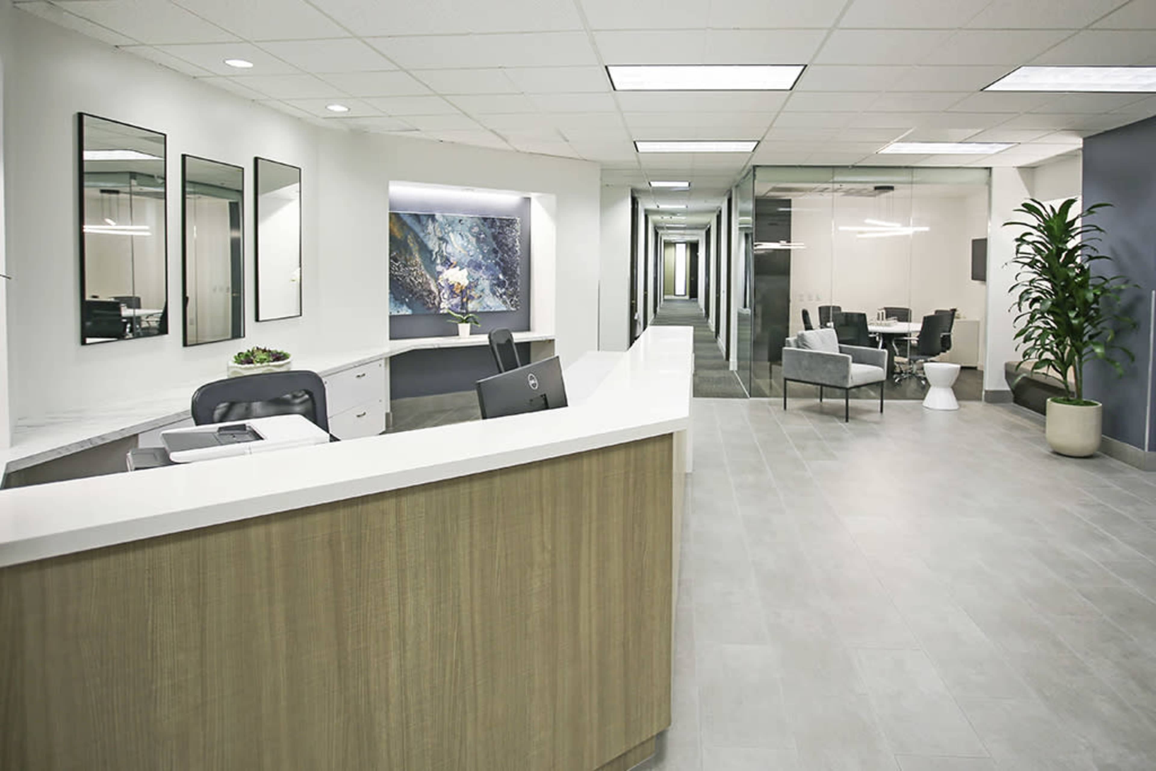 A modern office reception area with a front desk, multiple mirrors on the wall, and glass partitions leading to a meeting space.