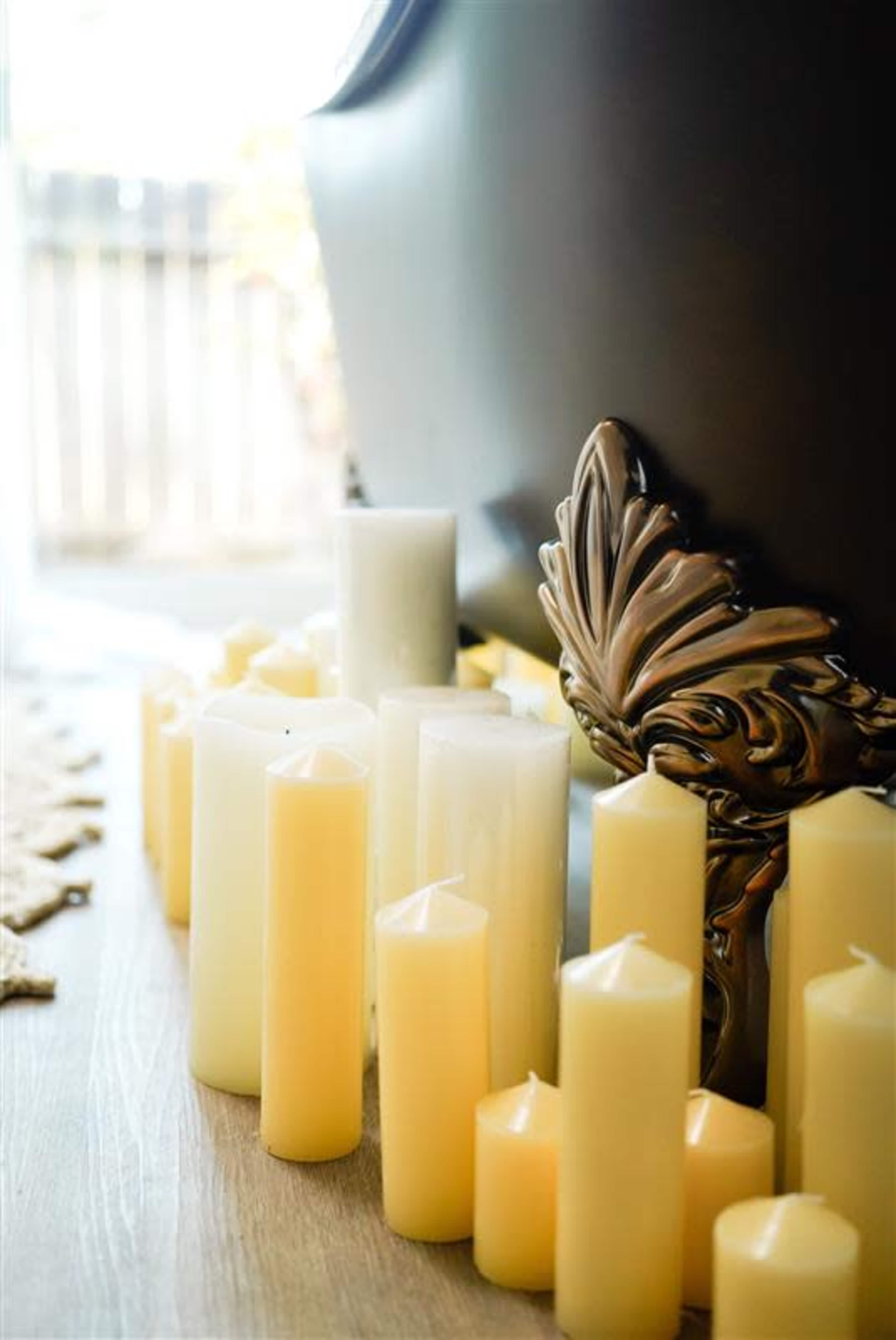 A collection of white and yellow candles is arranged around the base of a vintage bathtub.