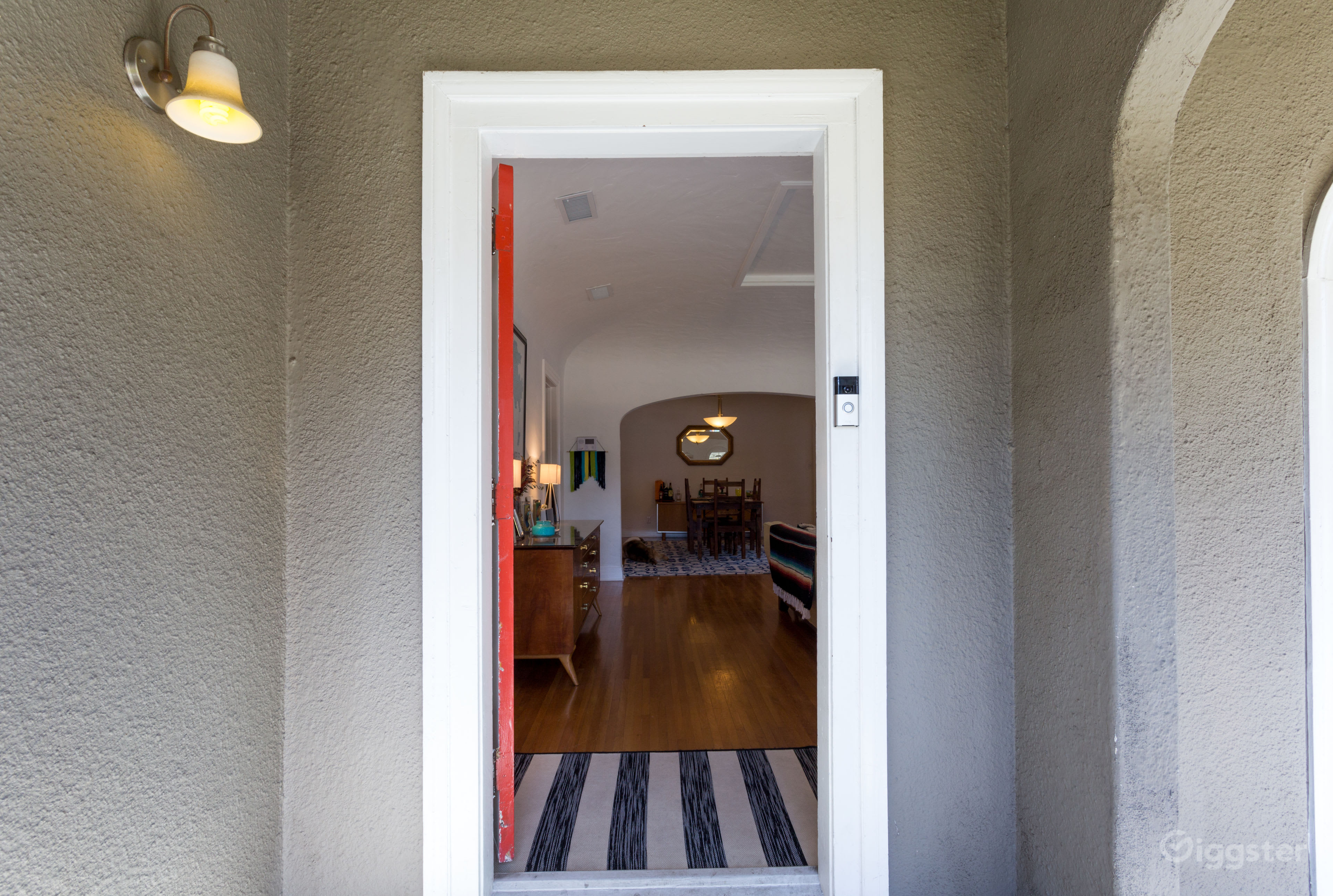 The image shows an open doorway with a view into a well-lit living room featuring wooden flooring and a dining area in the background.