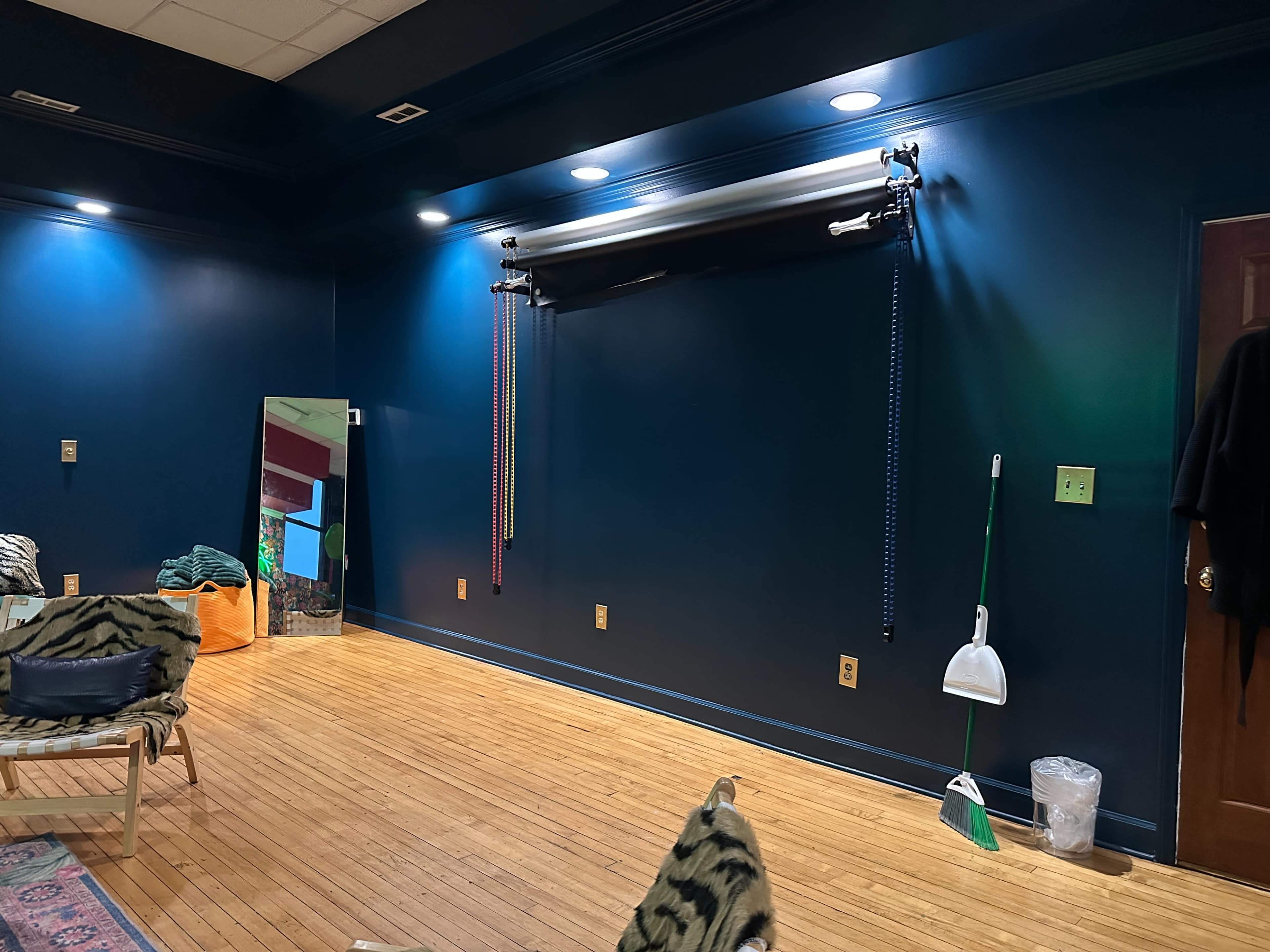 The image shows a room with dark blue walls, wooden flooring, and a storage area featuring a mirror and hanging equipment on the wall.