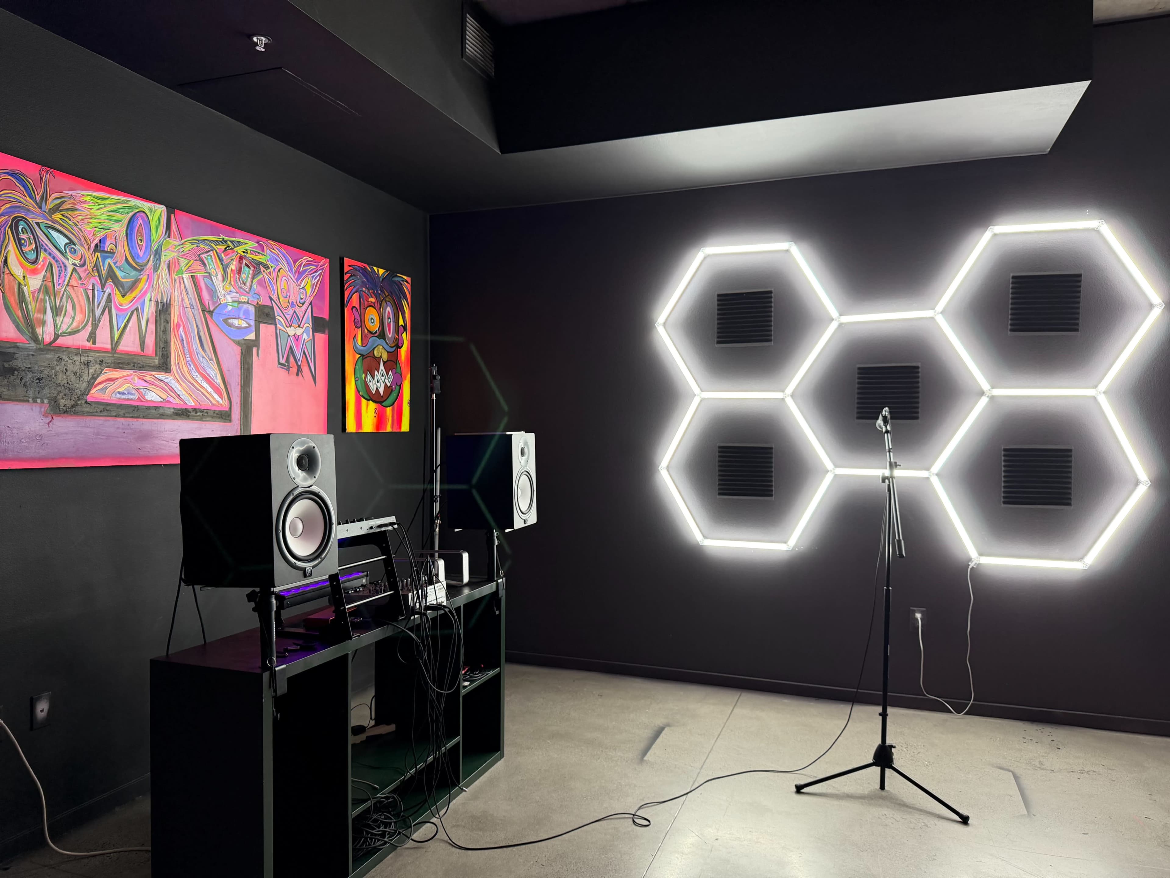 The image shows a modern music studio with colorful abstract artwork on the wall, a speaker setup, and a microphone stand illuminated by hexagonal LED lights.