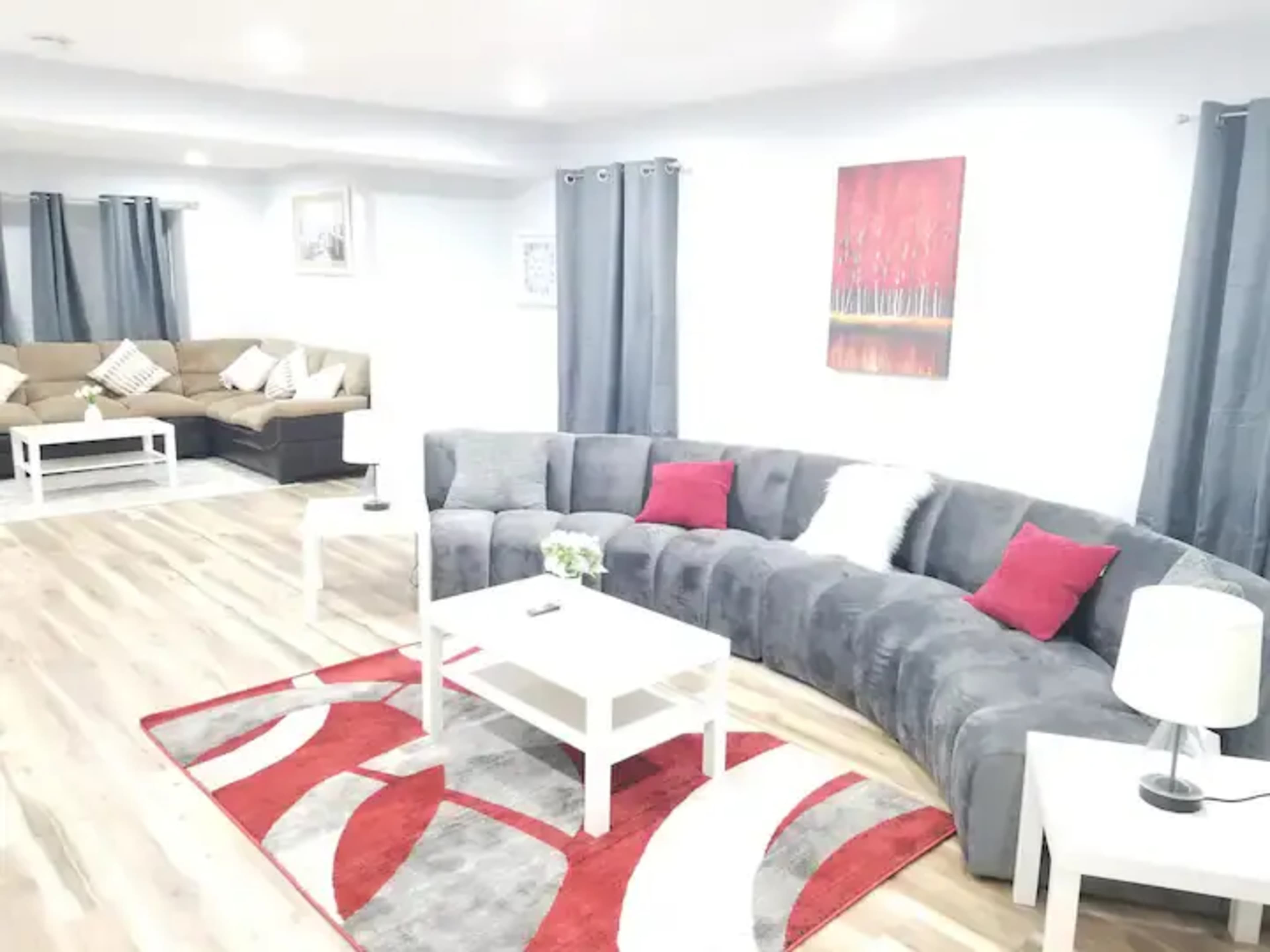 A modern living room featuring a curved gray sofa, a white coffee table, and decorative accents, with red and gray rugs on a wooden floor.