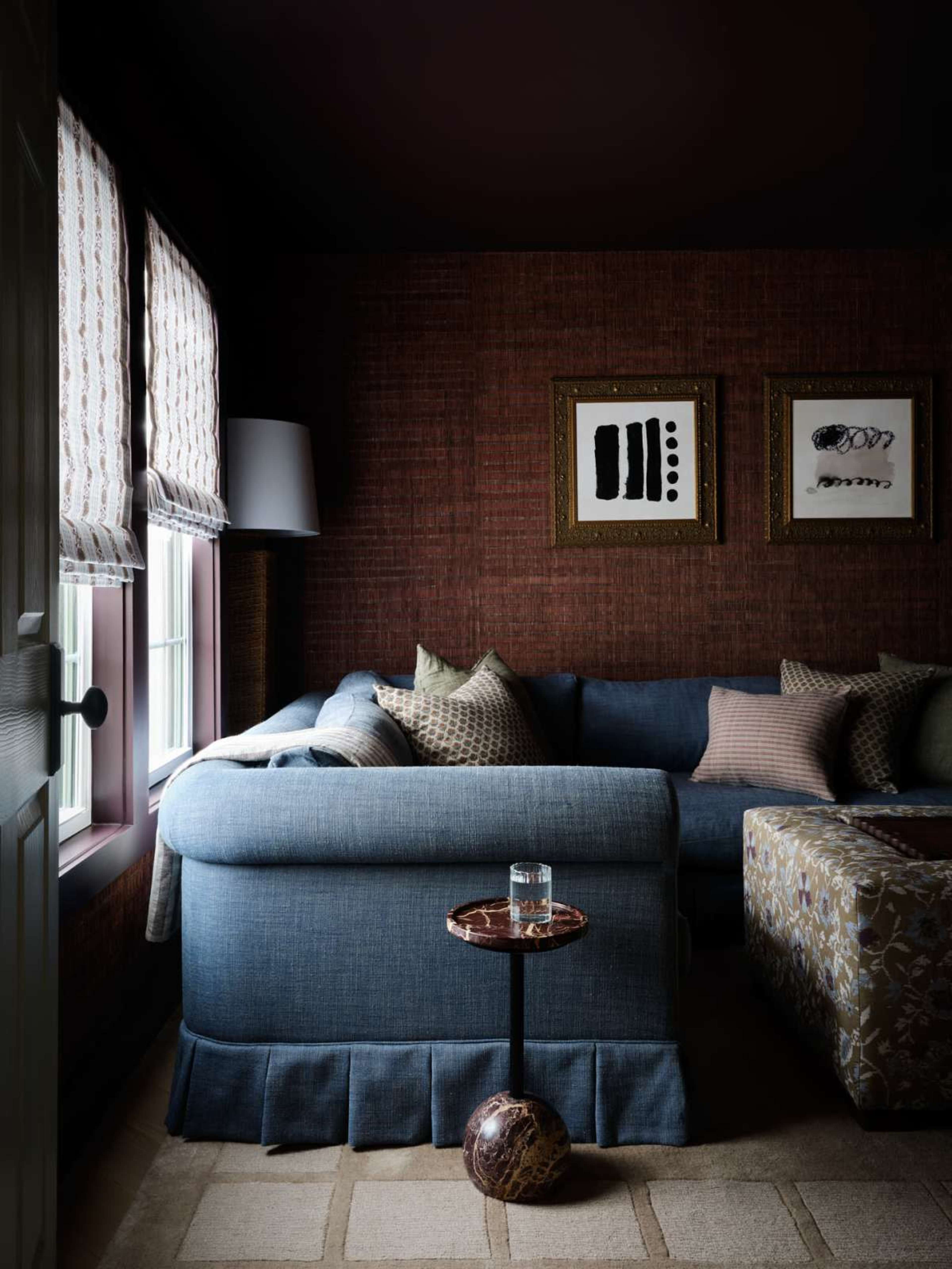 A cozy corner features a blue sofa with patterned pillows, a small side table, and framed art on a textured wall.