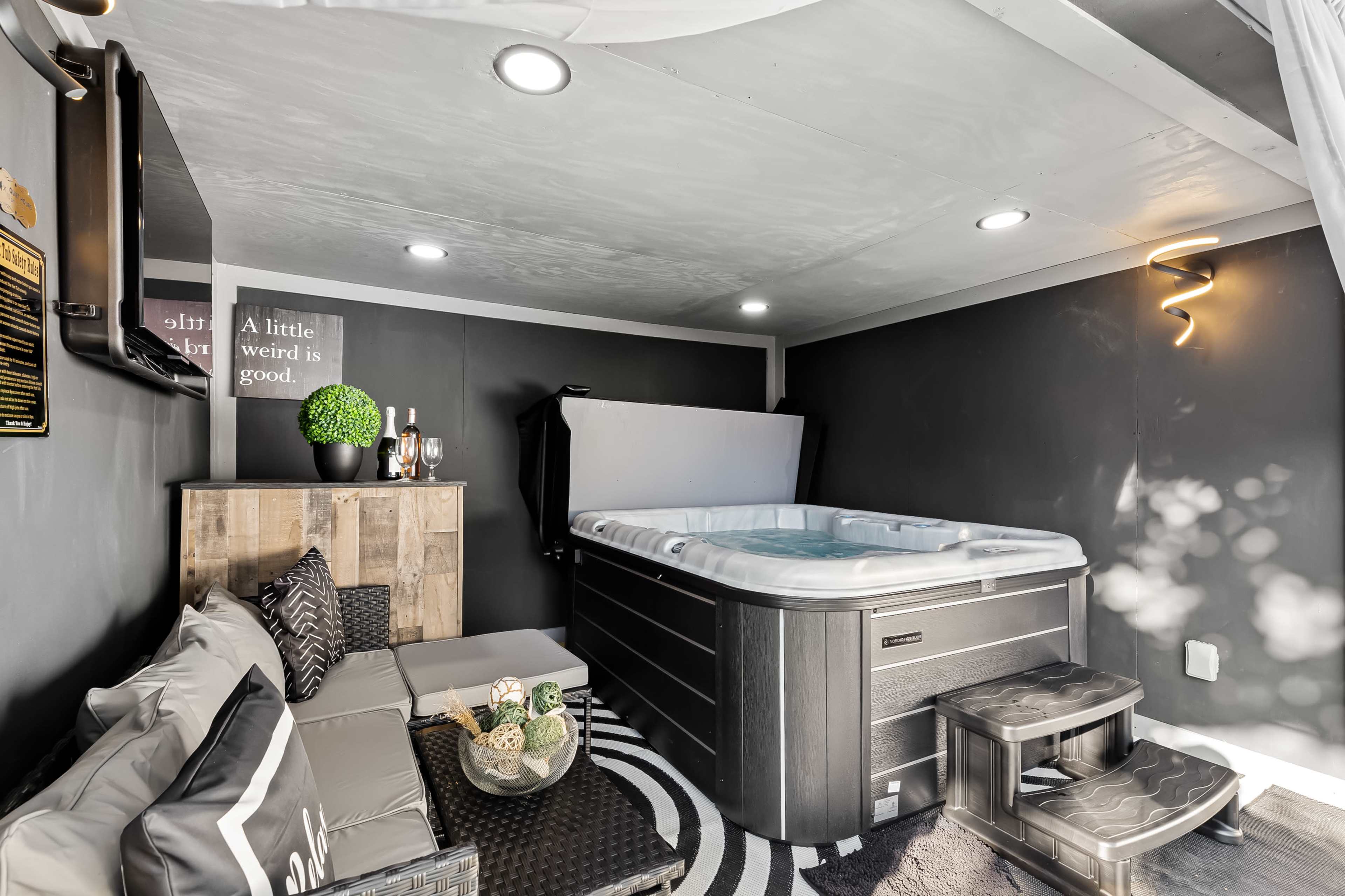 The image depicts a modern spa room featuring a hot tub, seating area with a coffee table, and contemporary decor.