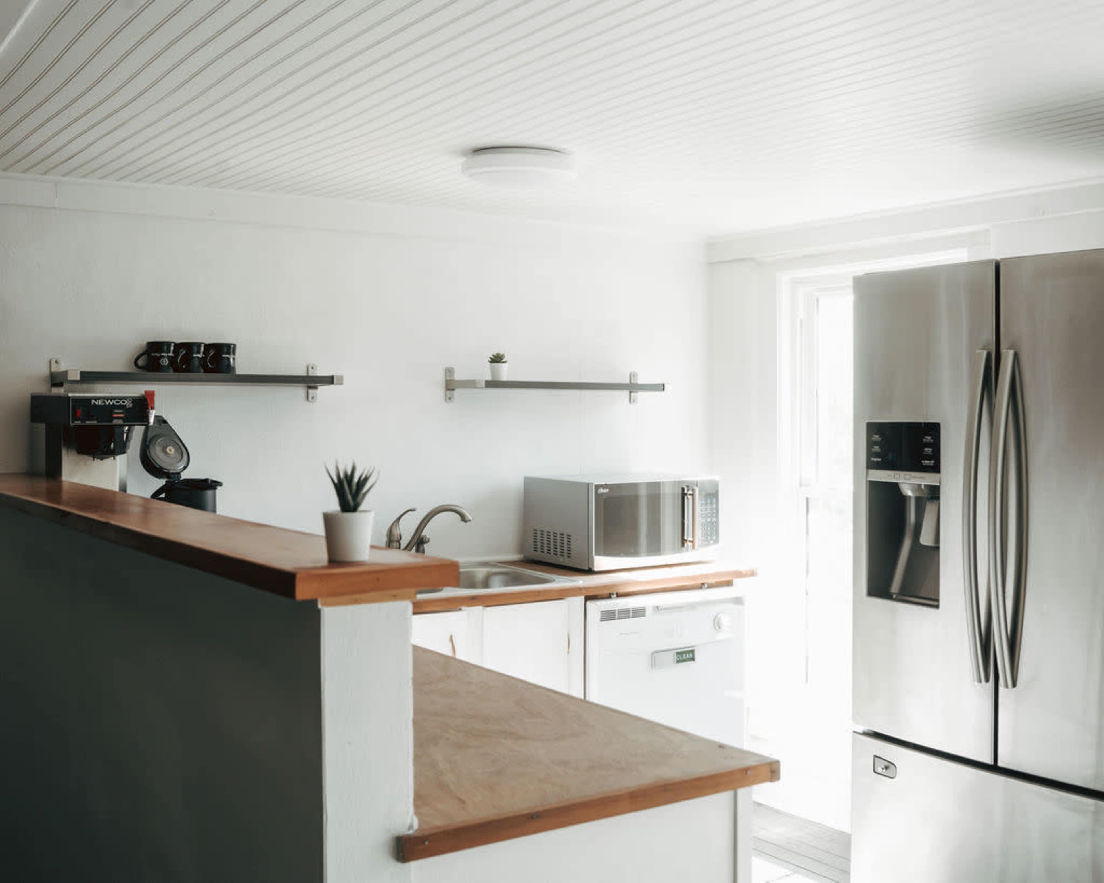 The image shows a modern kitchen with stainless steel appliances, open shelves, and a simple countertop layout.