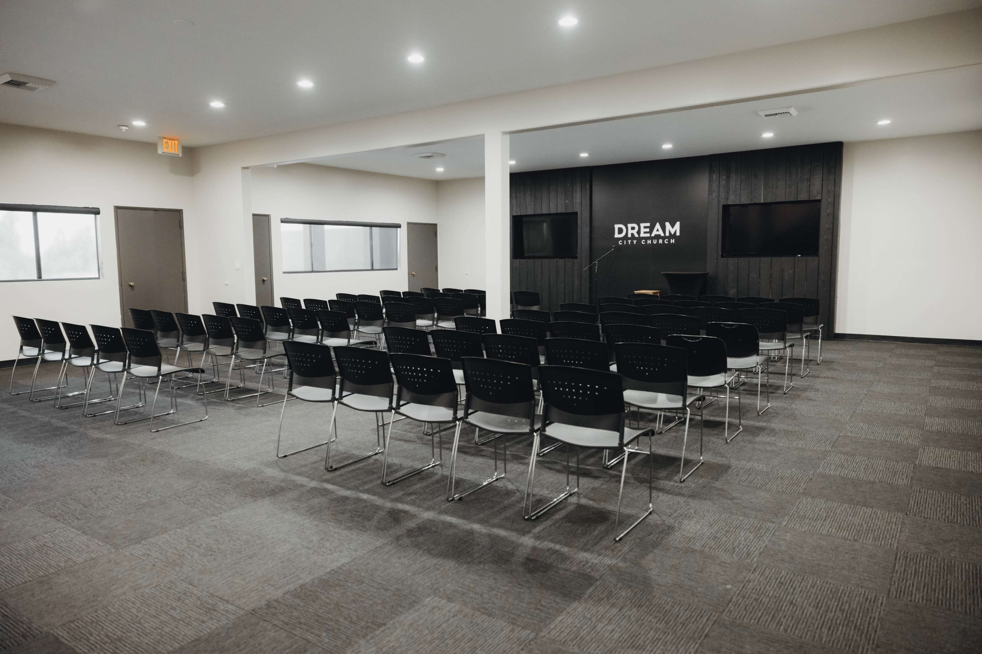 The image shows a spacious meeting room with neatly arranged rows of black chairs facing a screen and a dark wood-paneled wall displaying the word "DREAM."