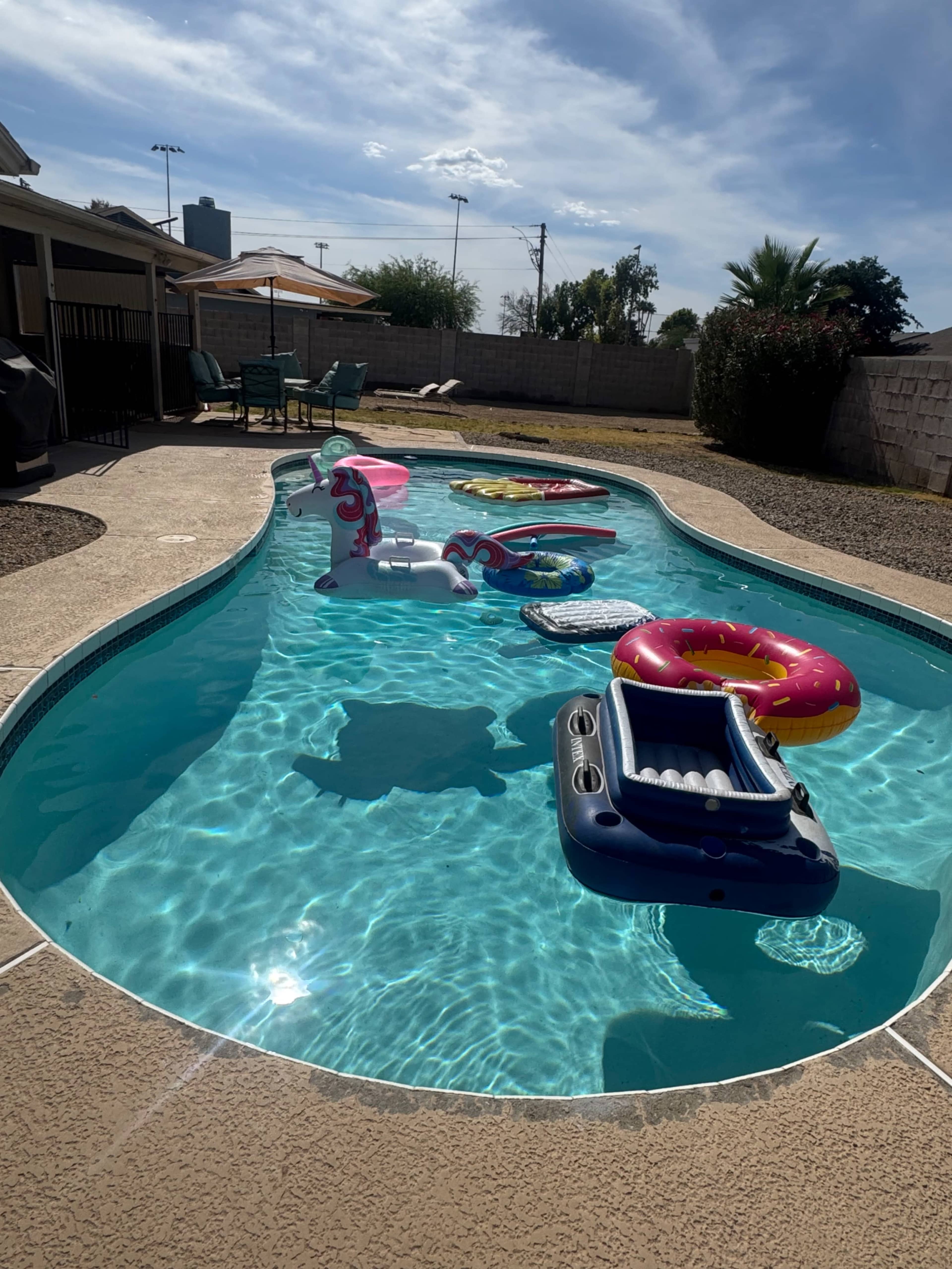 An assortment of inflatable pool floats in various shapes and colors is floating on the water of a curved swimming pool.