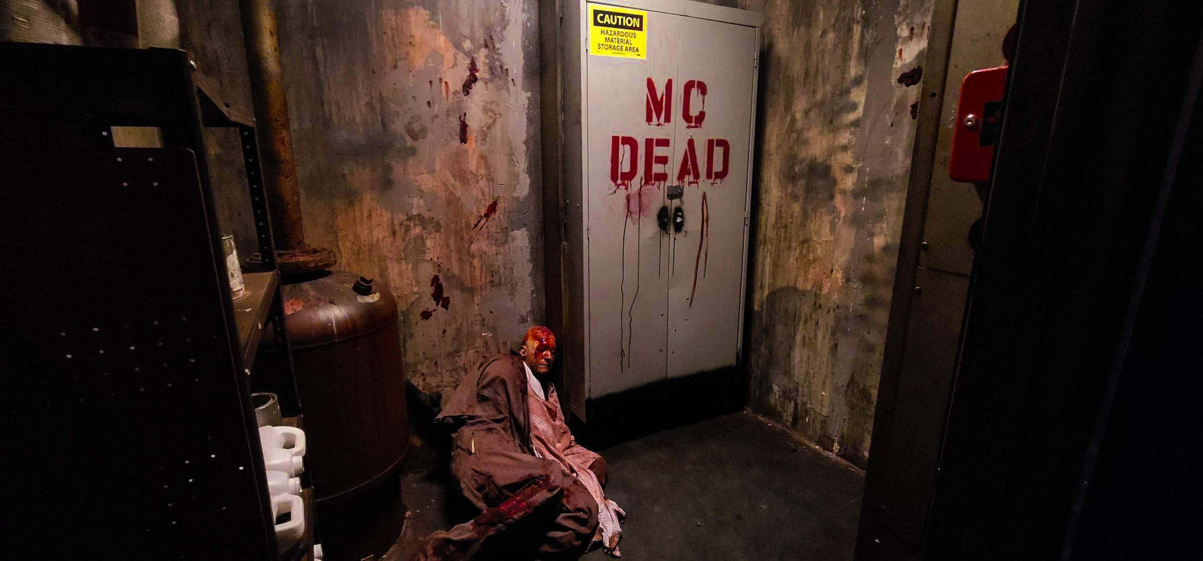A dimly lit corridor features a door labeled "MC DEAD," with blood splatters on the walls and a figure lying on the ground.
