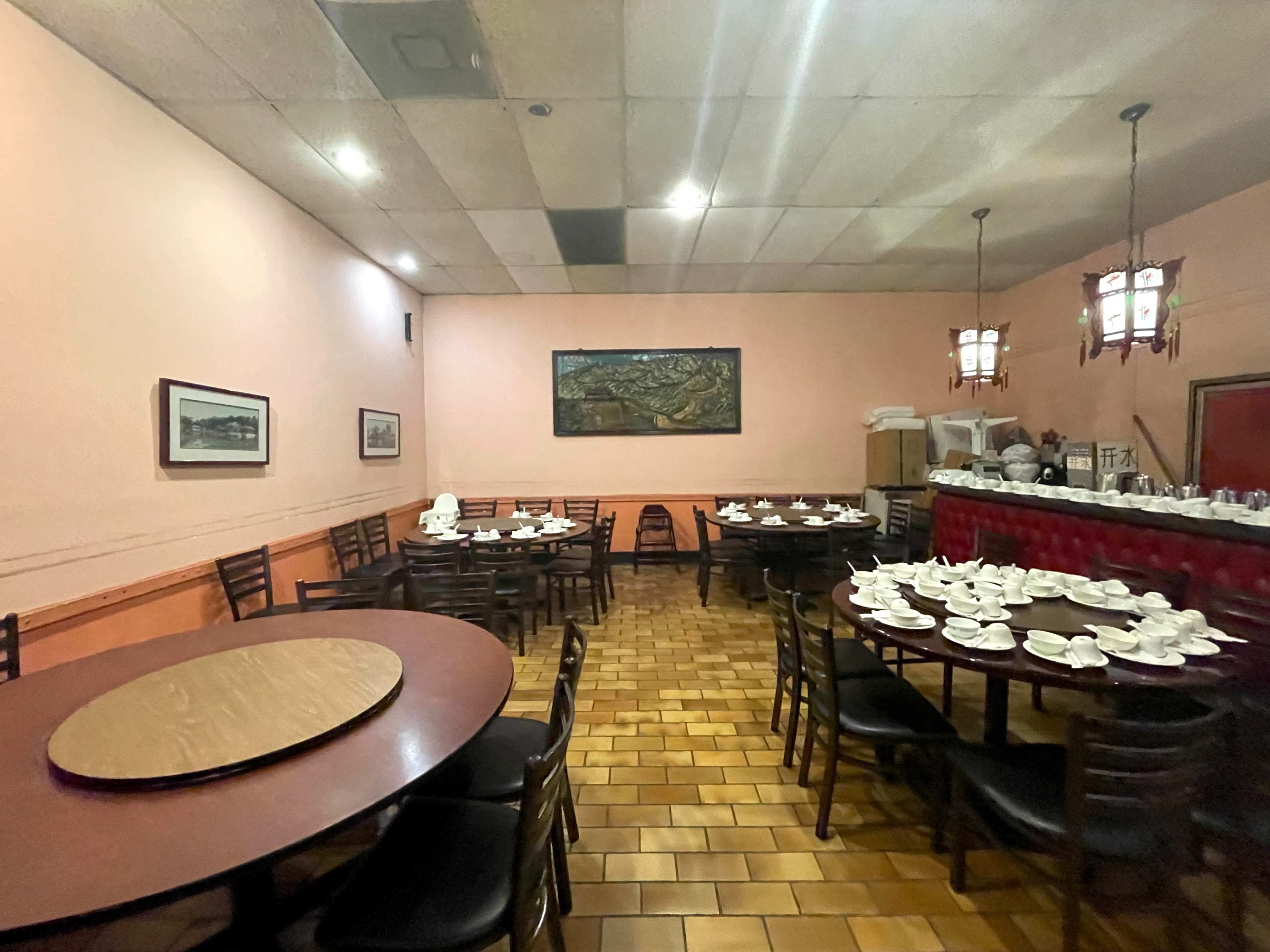 The image shows a dining area with multiple round tables set with tea cups, surrounded by pink walls and a framed painting.