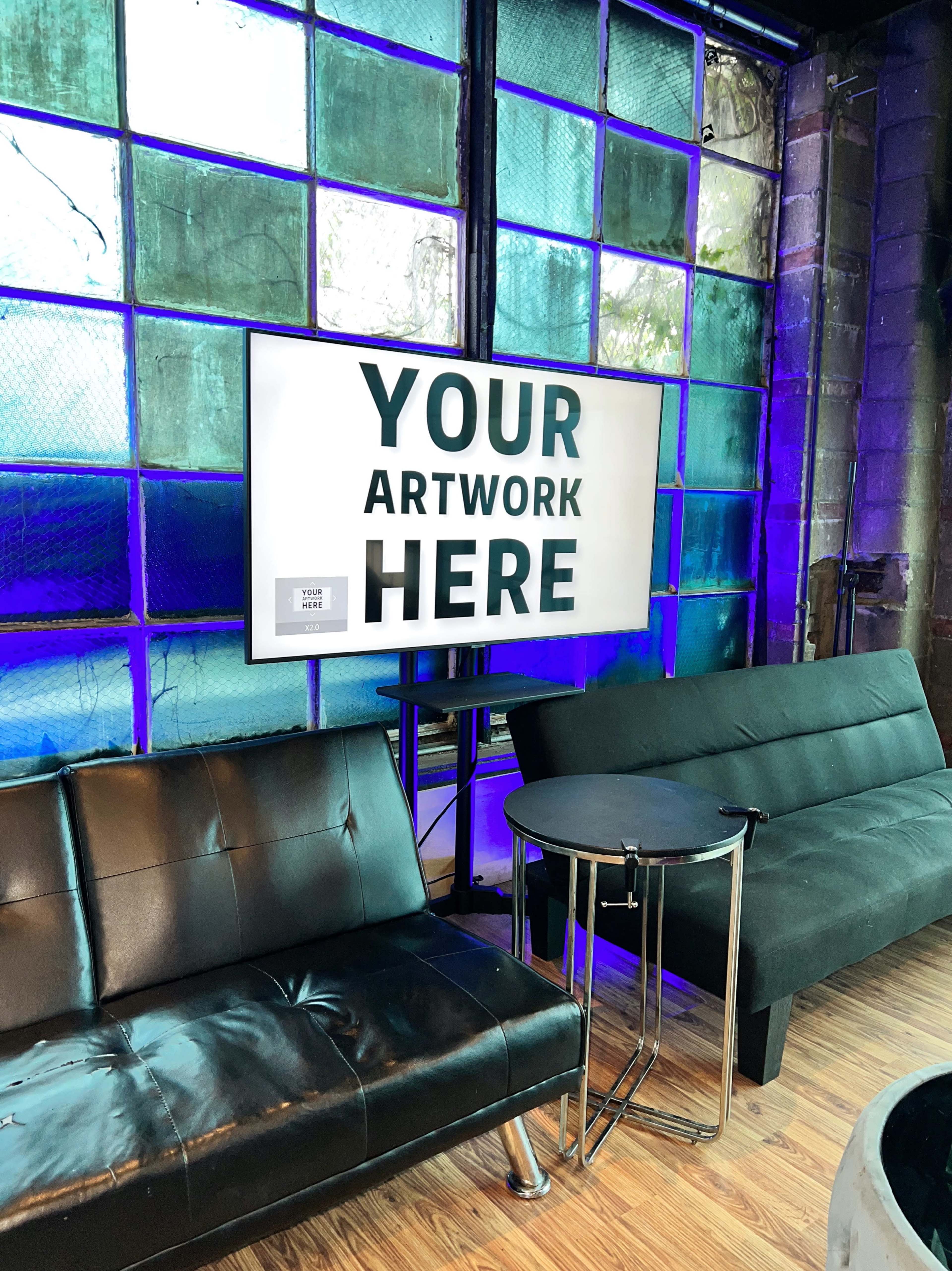 A black leather couch and a small round table are positioned in front of a large digital display surrounded by colorful stained glass windows.