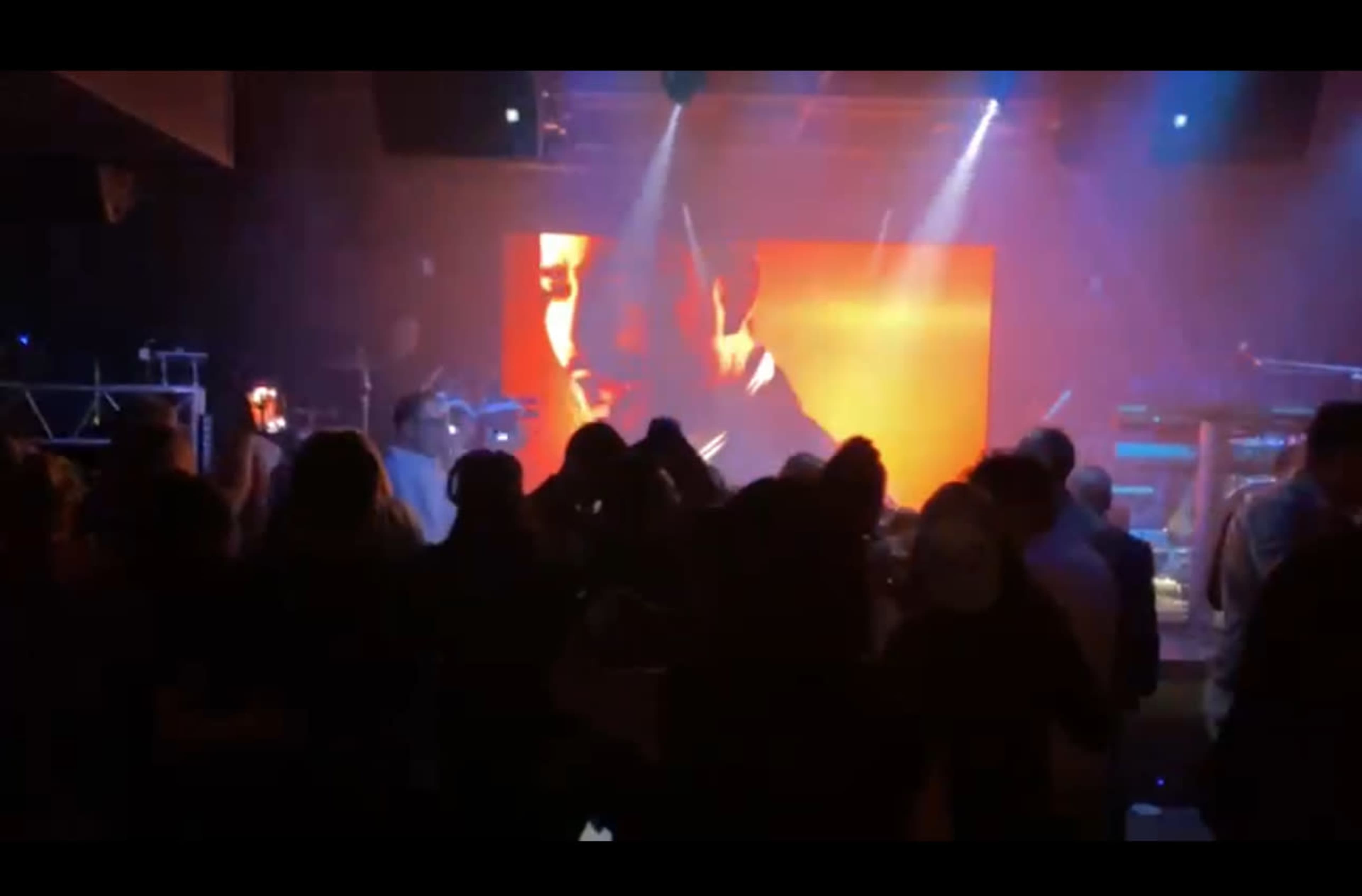 A crowd enjoys a live performance while a large screen displays a close-up of a performer.