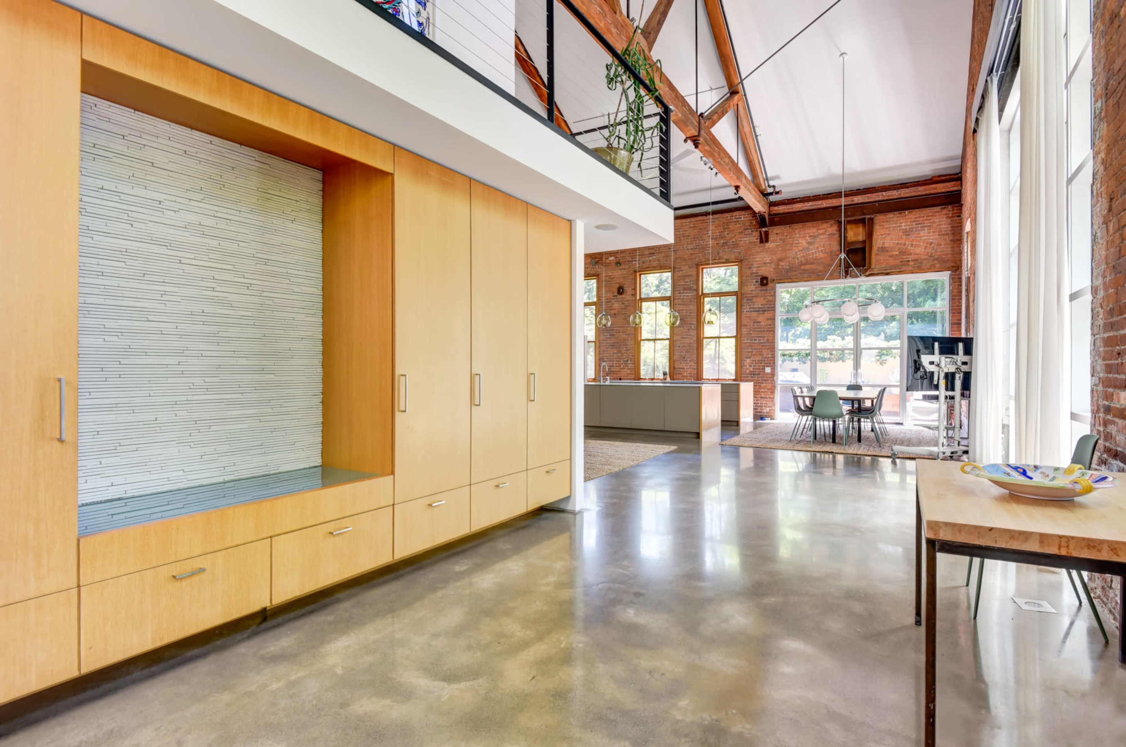 A modern interior space featuring a wooden cabinetry unit, large windows, and an open layout connecting to a dining area.