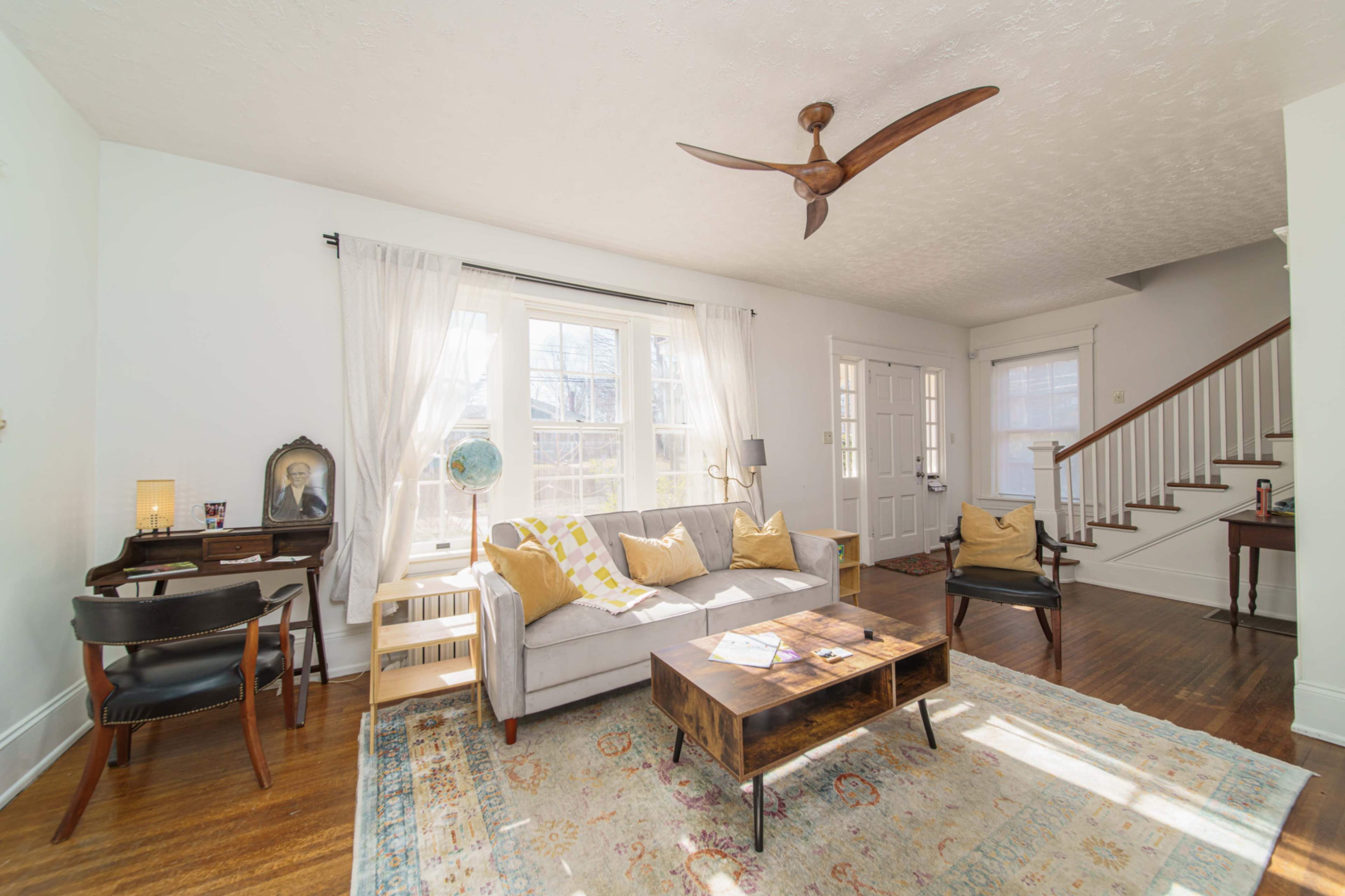 The living room features a gray sofa with yellow and white pillows, a coffee table, and a staircase in the background.