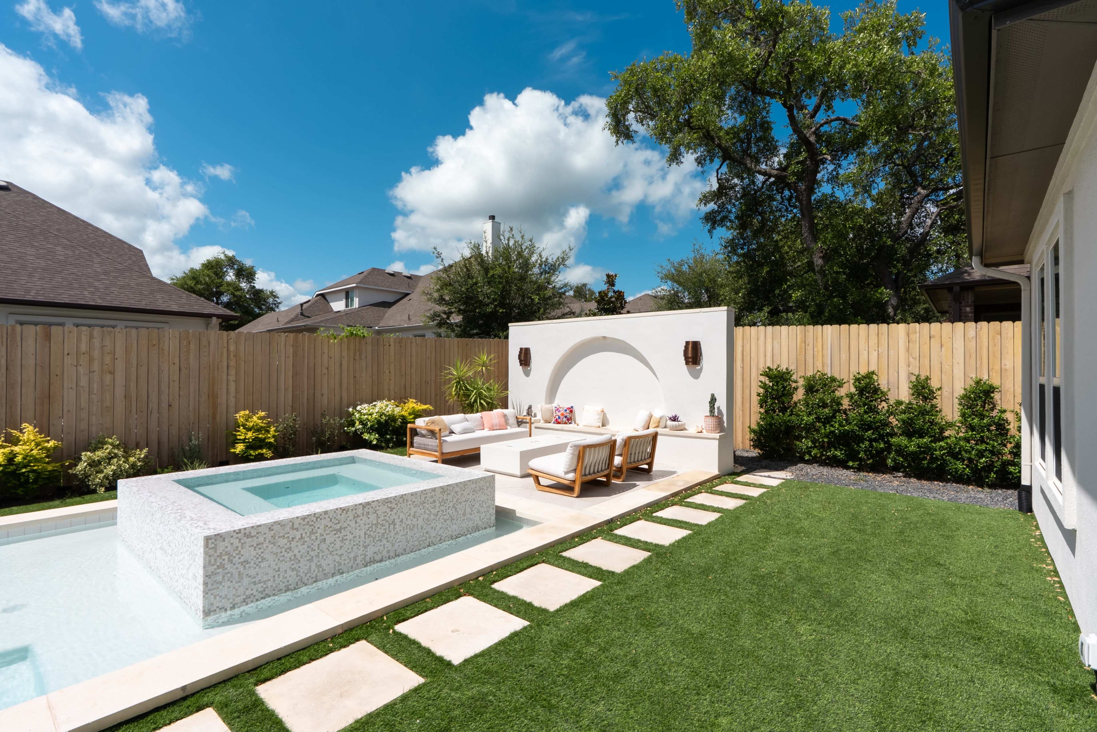 A landscaped backyard features a concrete seating area, a small plunge pool, and a well-maintained lawn bordered by a wooden fence.