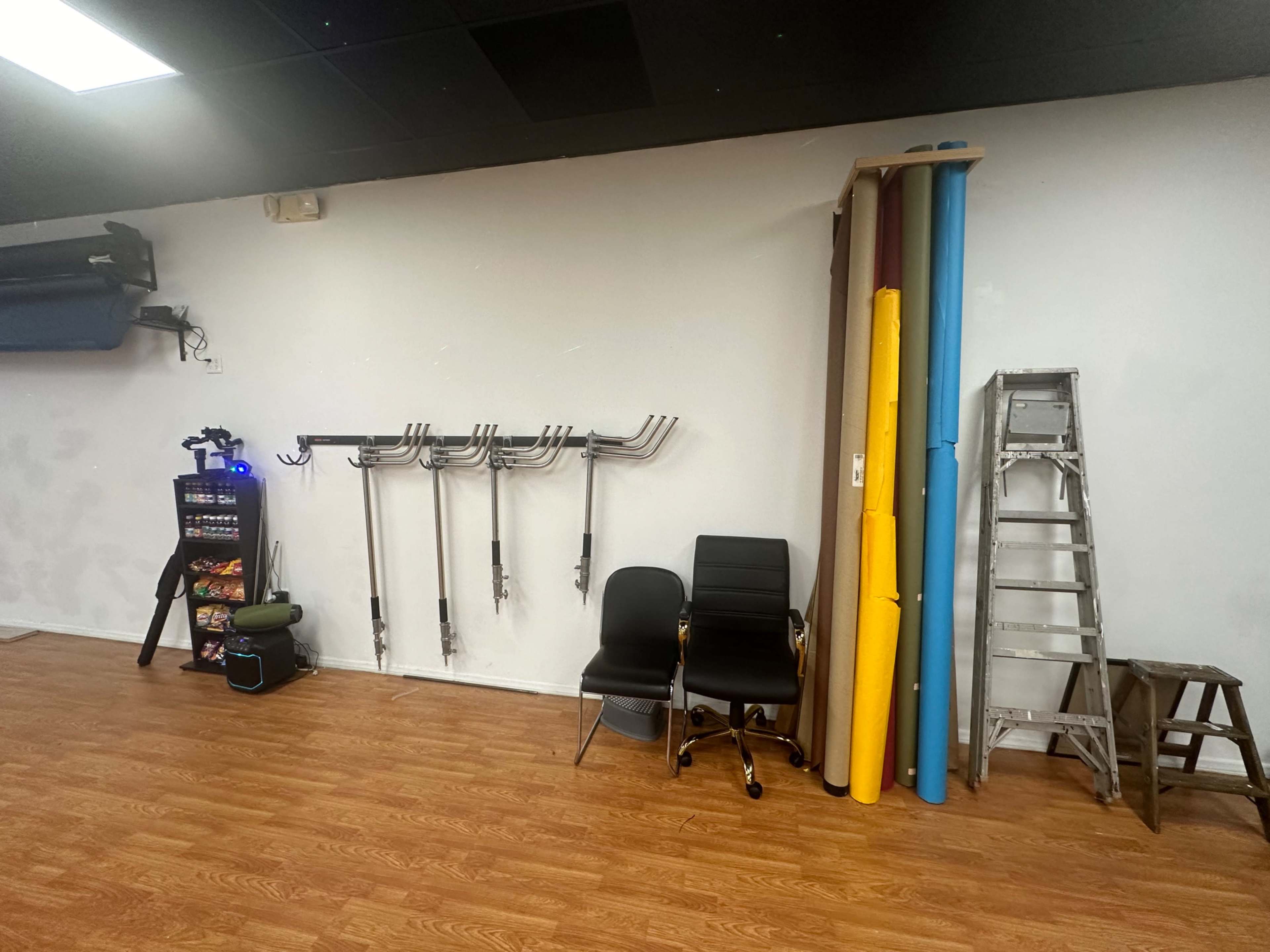 A wall with several exercise mats in various colors, two black chairs, a ladder, and a vending machine in a fitness or training space.