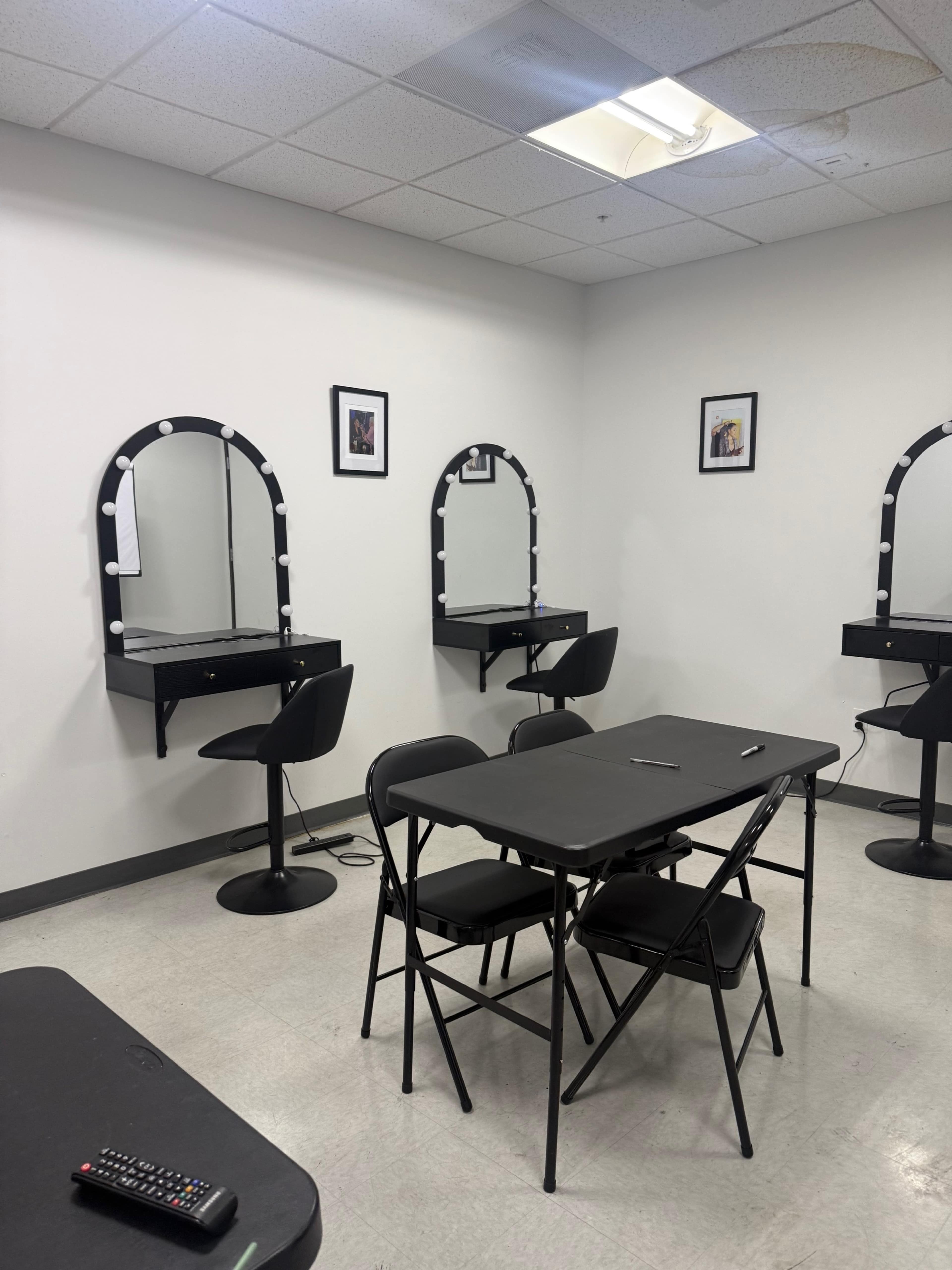 The image shows a small room with two mirror stations and a table surrounded by folding chairs.
