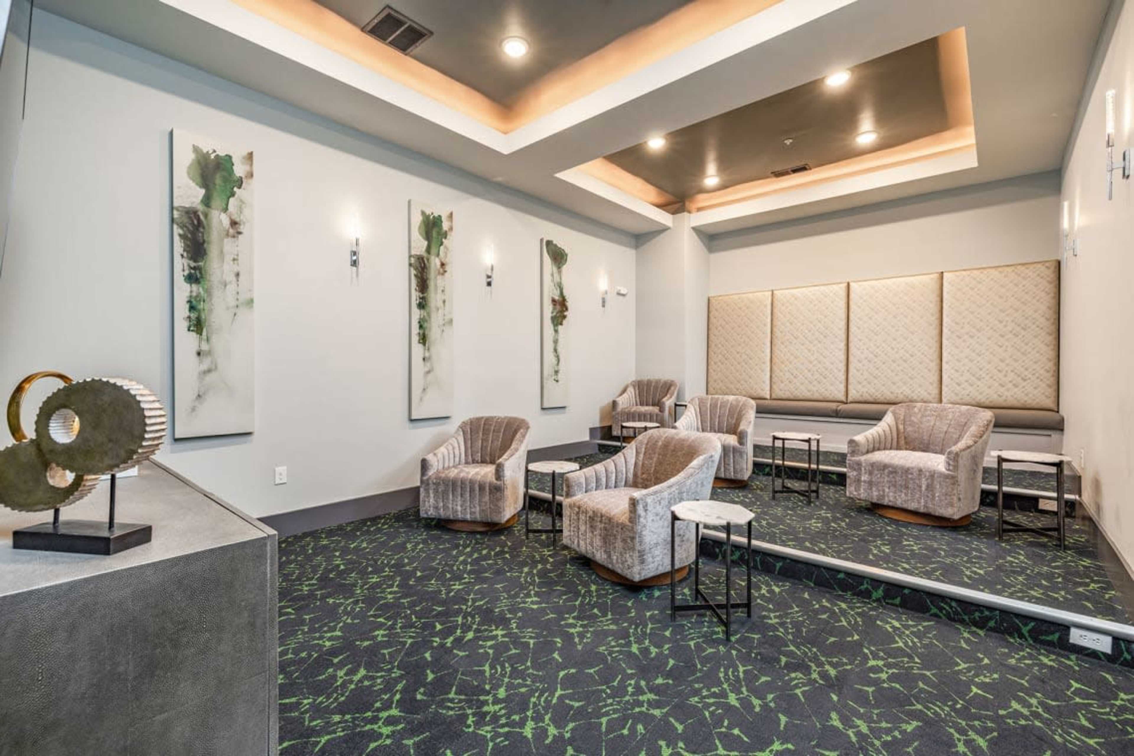 The image shows a modern lounge area with four armchairs, decorative wall art, a textured back wall, and a dark green patterned carpet.
