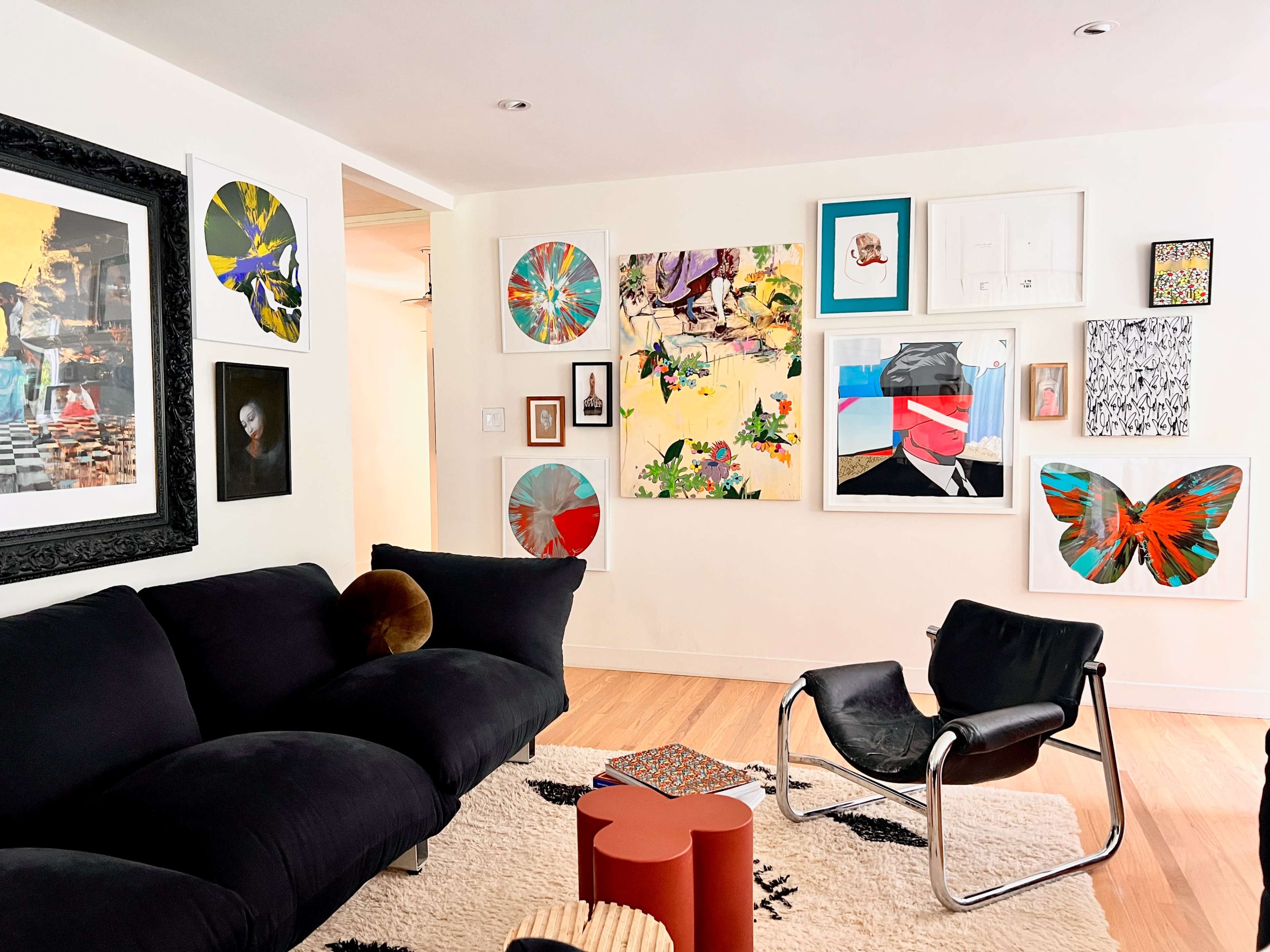 A cozy living room features a black sofa and a contemporary chair, with a colorful gallery wall of framed art and photographs.