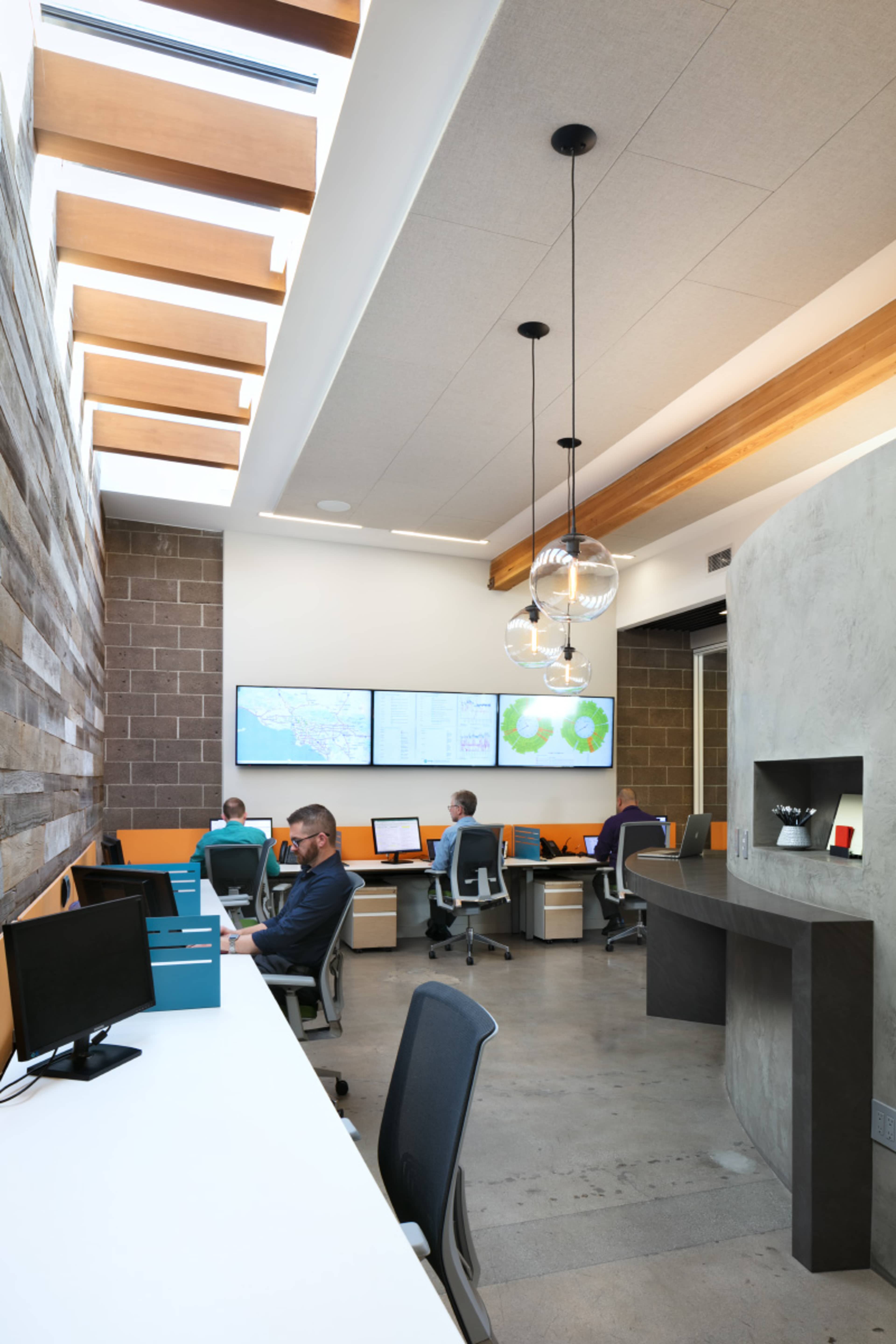 A modern office space with multiple workstations, large screens displaying data, and a mix of natural light and contemporary design elements.