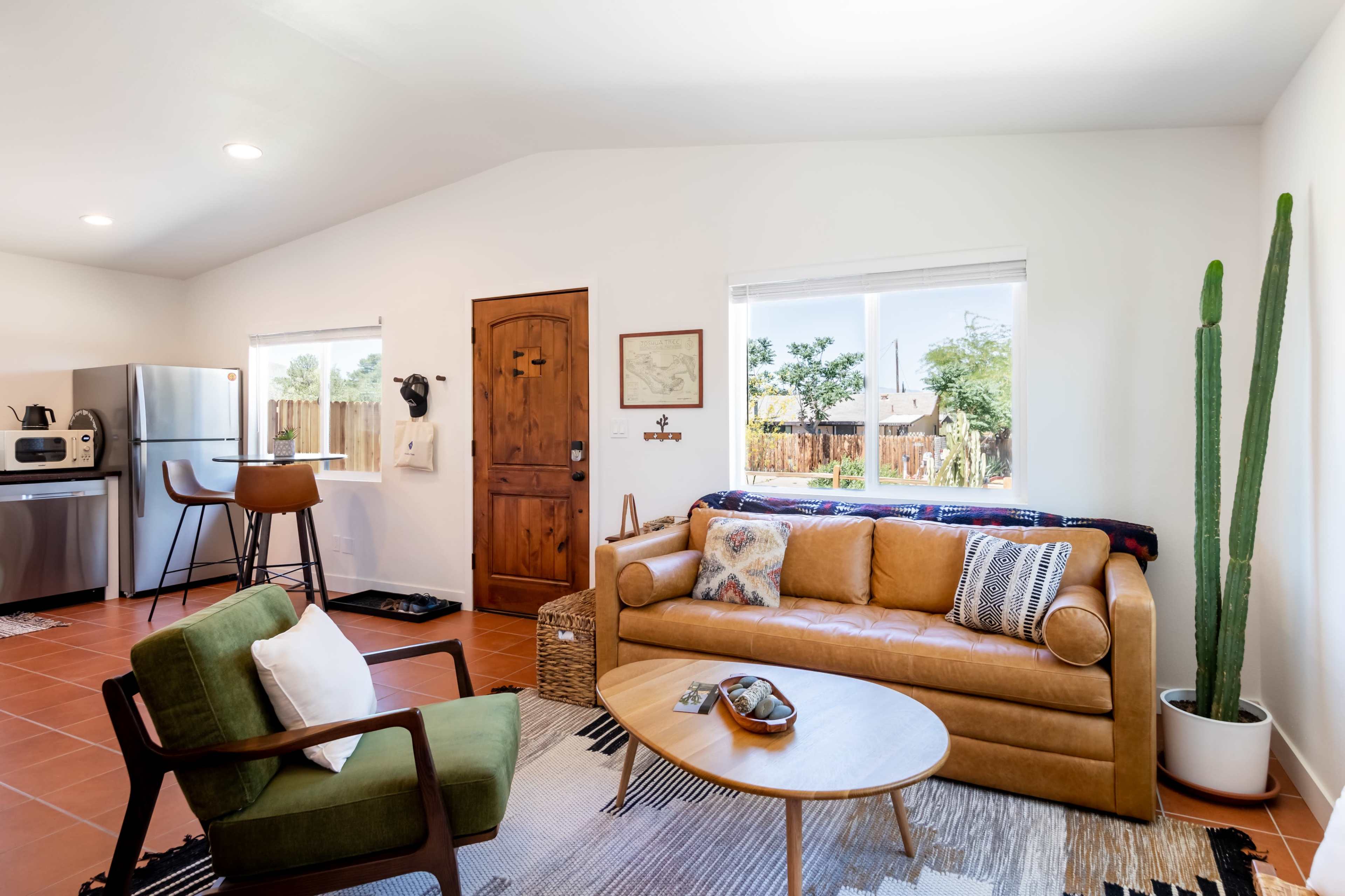 A cozy living space with a brown sofa, a green armchair, a round table, and a kitchen area visible in the background.