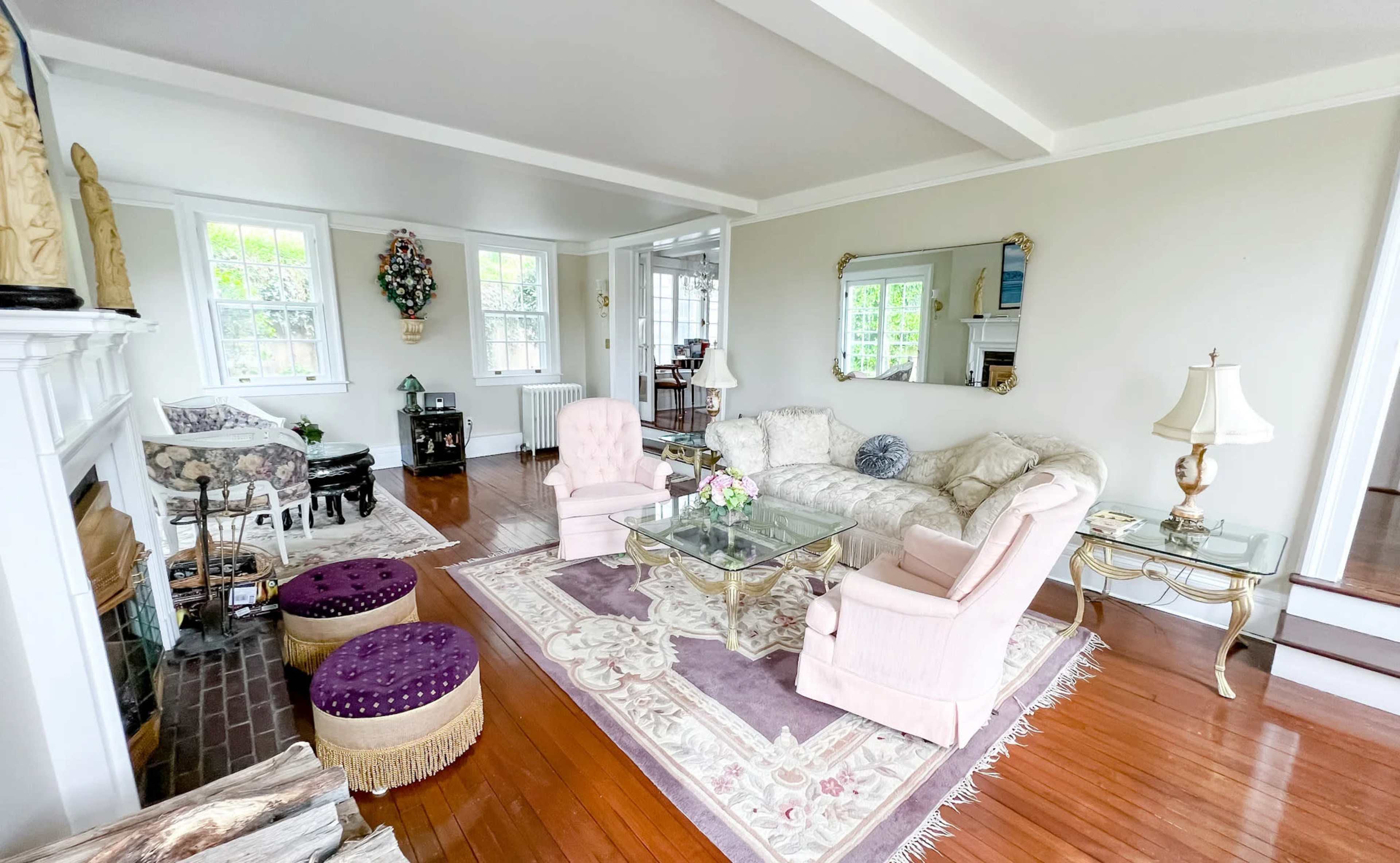 The living room features a light-colored sofa, two armchairs, a coffee table, and decorative accents, all set on polished wooden flooring.