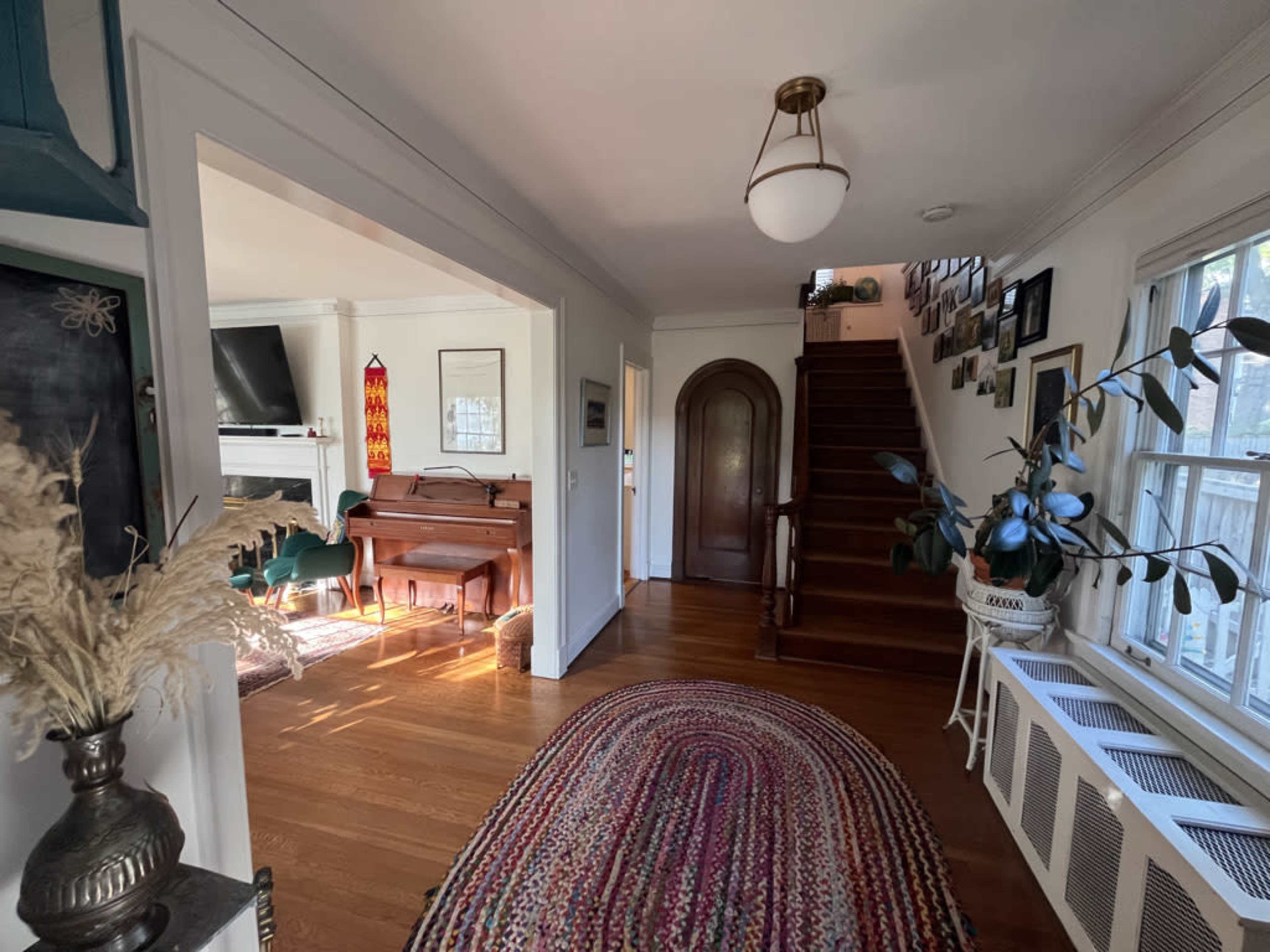 The image shows a hallway that leads to a staircase, with a piano in an adjacent room and various decorative elements along the walls.