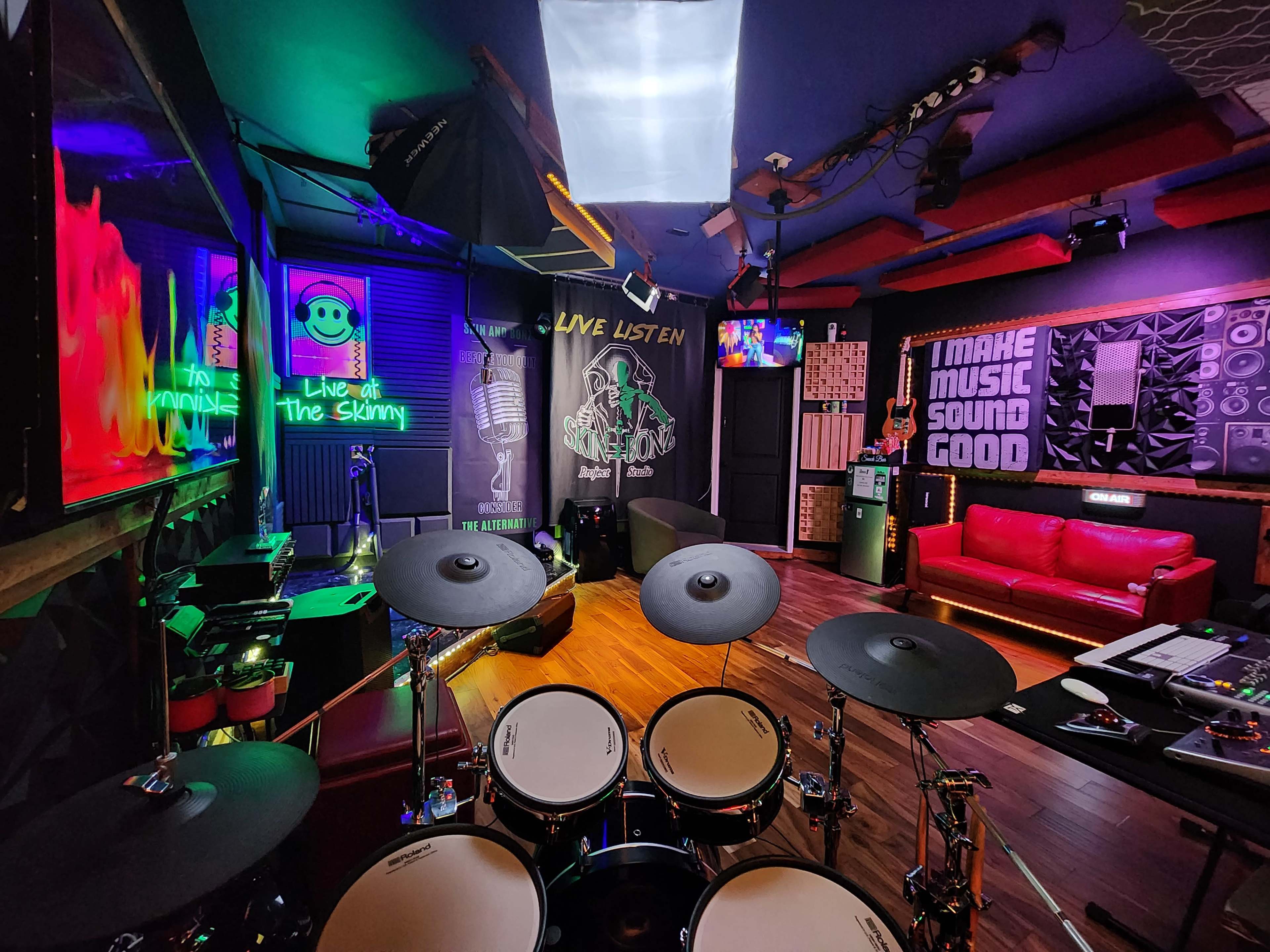 The image shows a vibrant music studio with a drum set in the foreground, colorful lights, and various music-themed decorations on the walls.